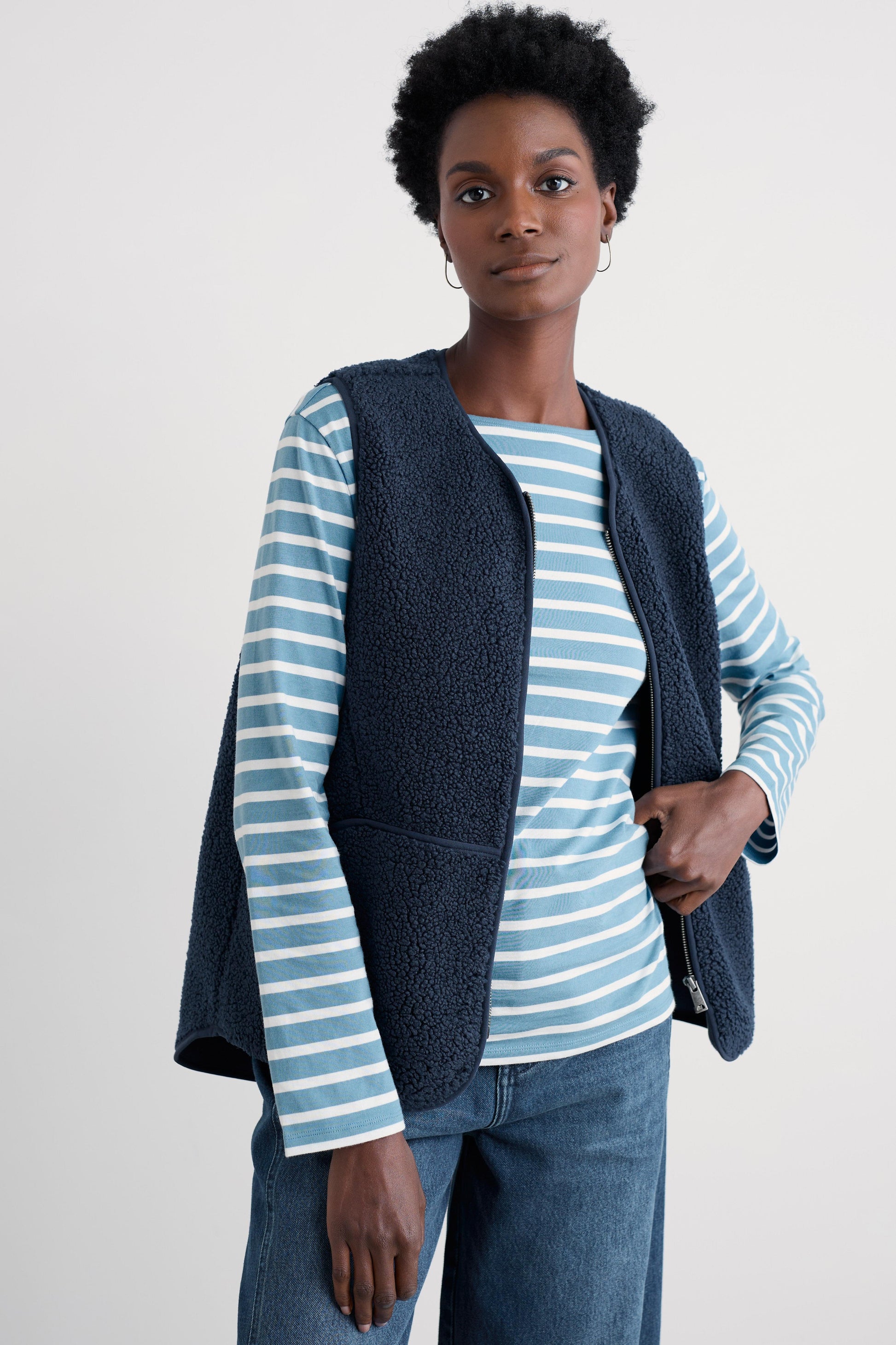 Woman wearing a blue striped shirt and dark blue vest against a white background