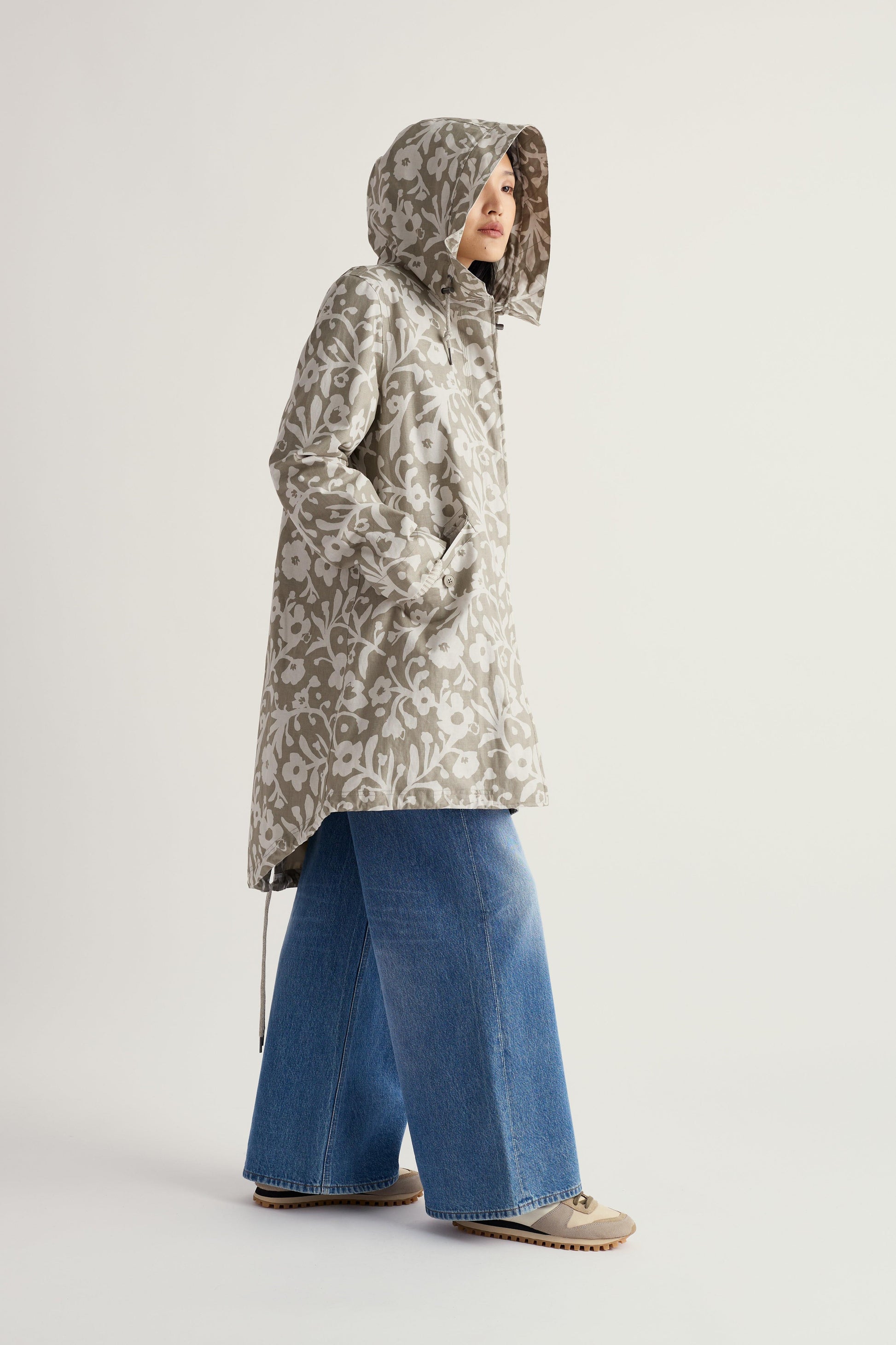 Person wearing a floral-patterned raincoat and blue jeans on a light gray background