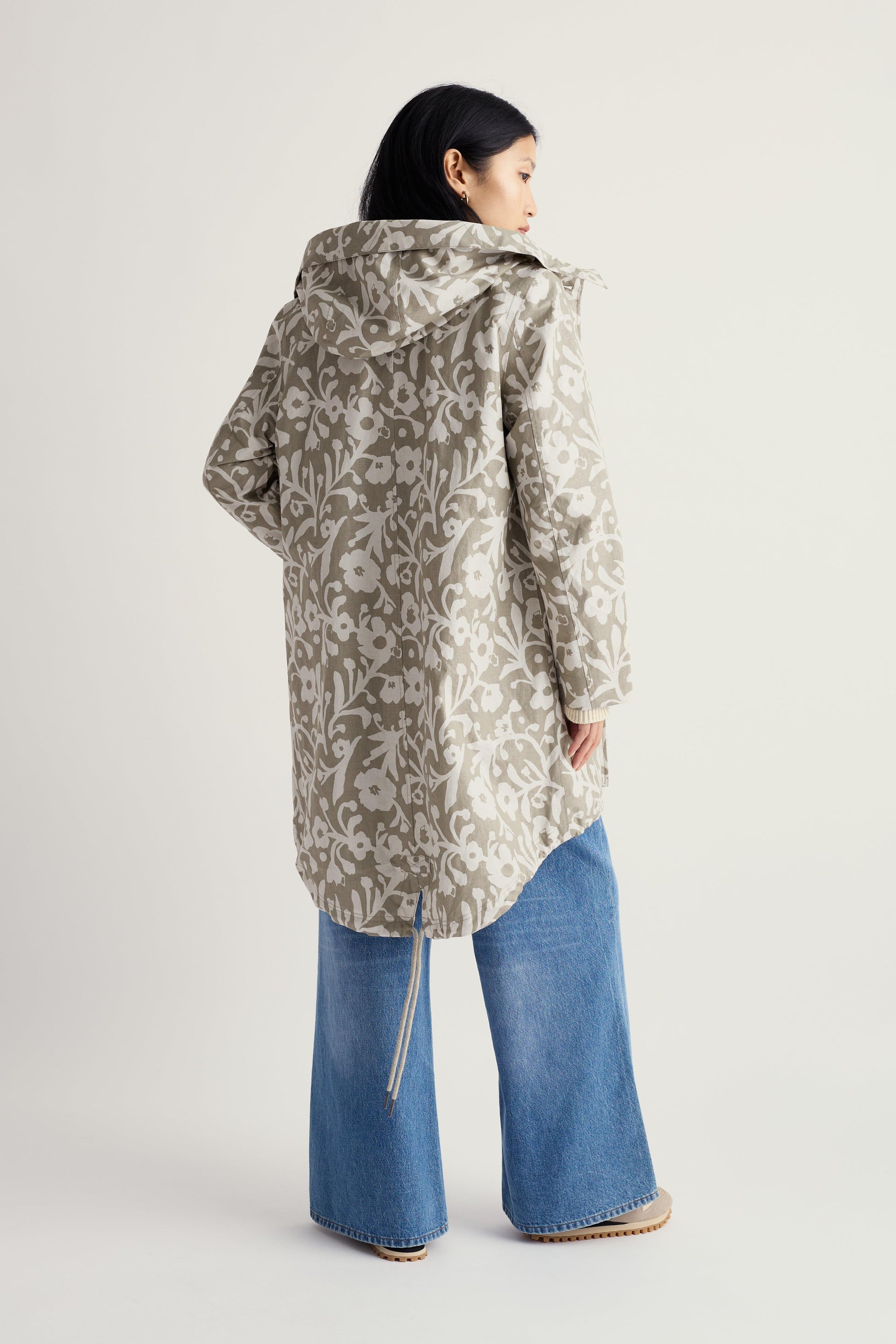 Person wearing a patterned coat and blue jeans on a white background