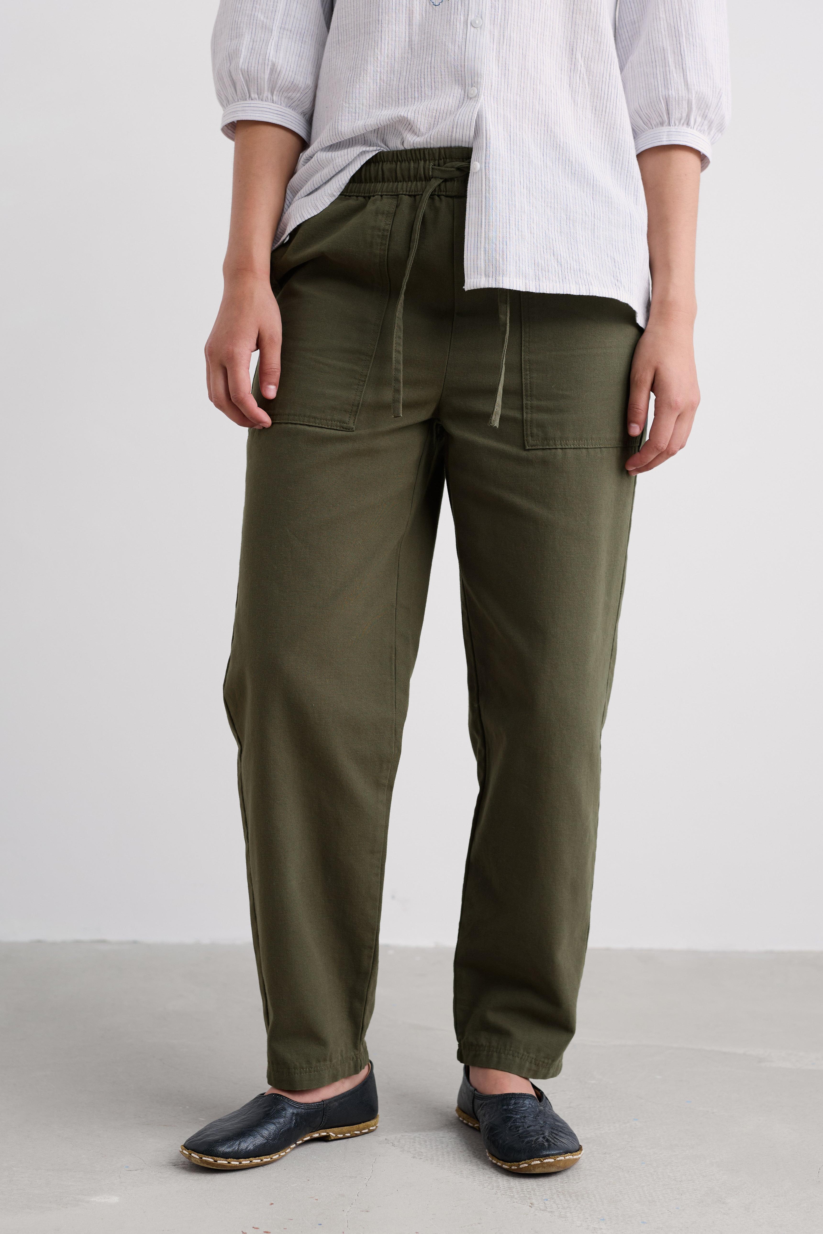 Person wearing olive green pants with a white shirt on a plain background