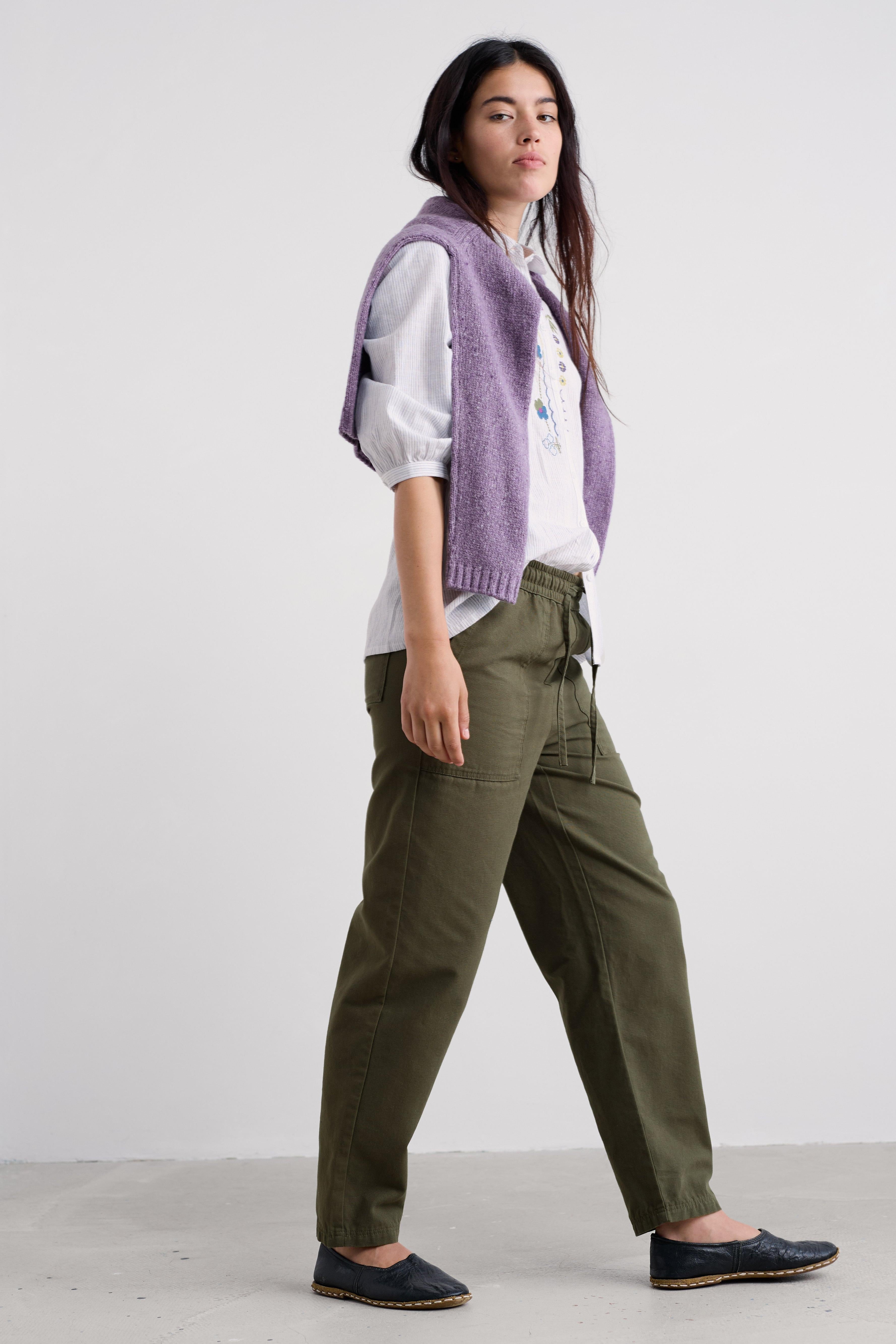Person wearing a purple vest, white shirt, and green organic cotton pants on a white background
