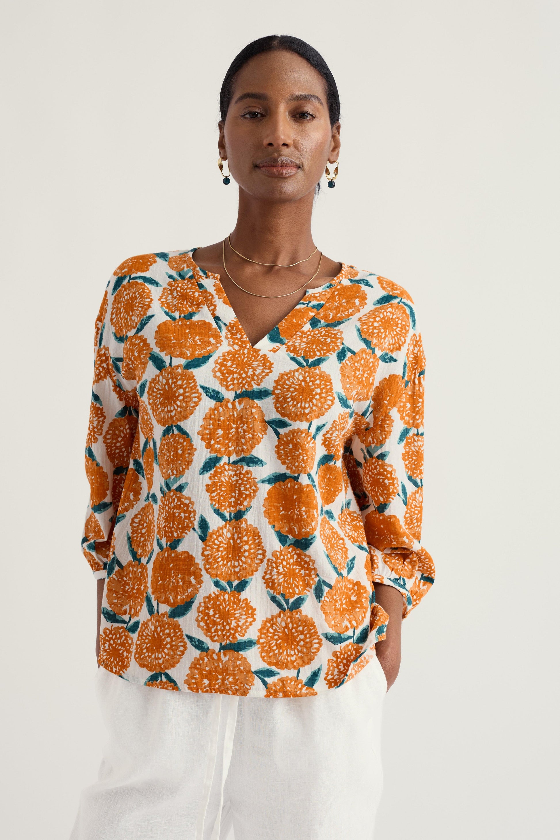 Woman wearing a patterned organic cotton blouse with orange and green design on a white background