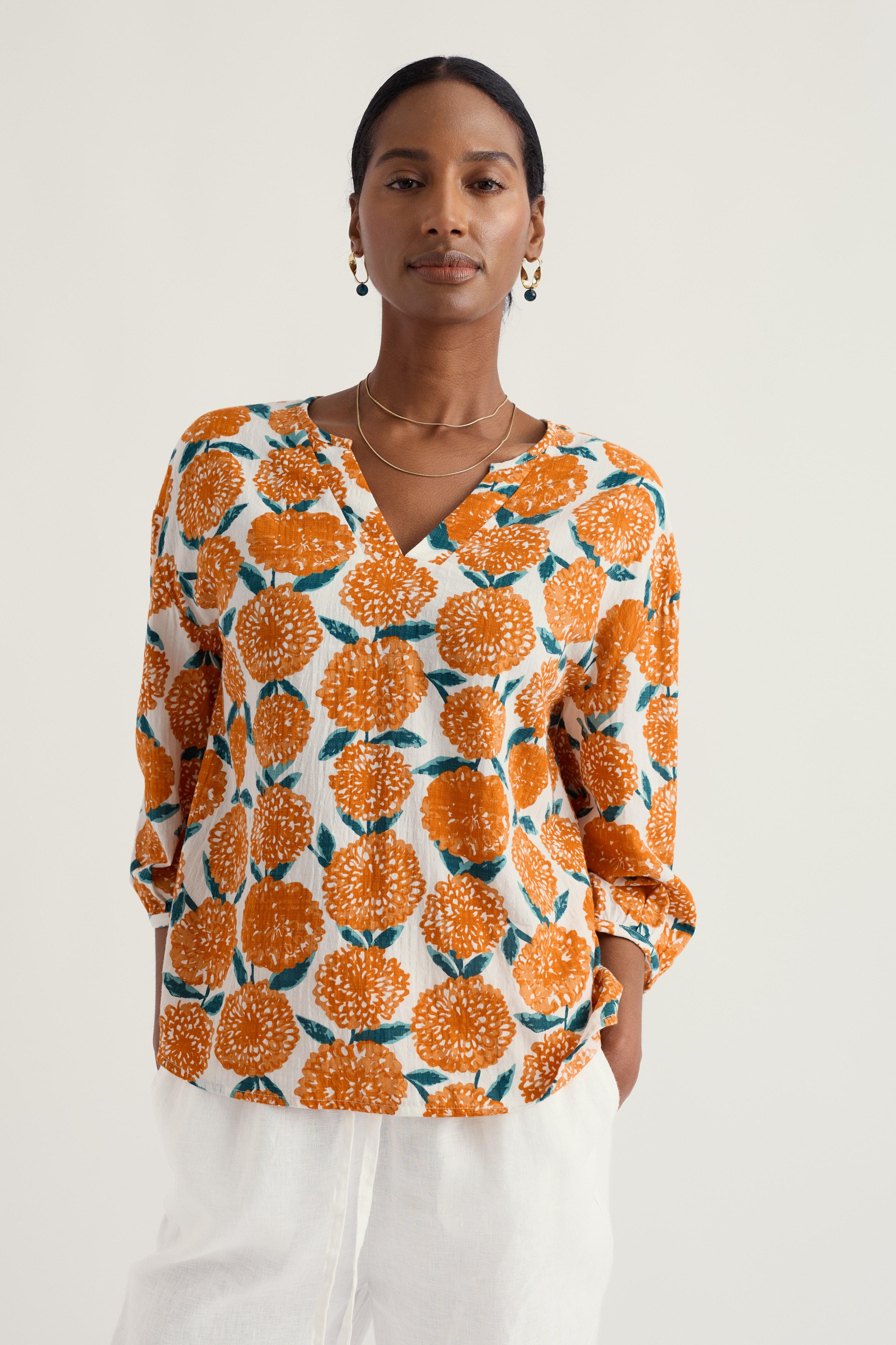 Woman wearing a patterned organic cotton blouse with orange and green design on a white background