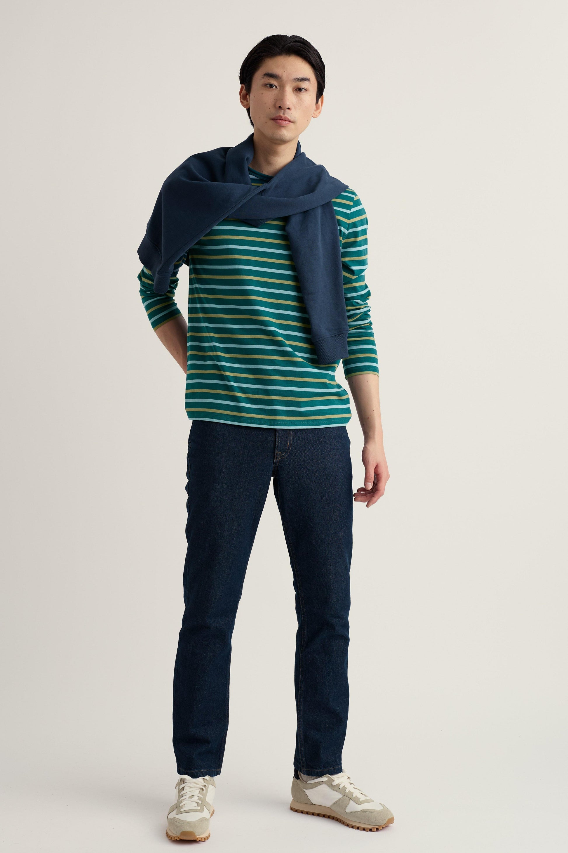 Man wearing a striped organic cotton top and navy pants with a blue scarf on a plain background