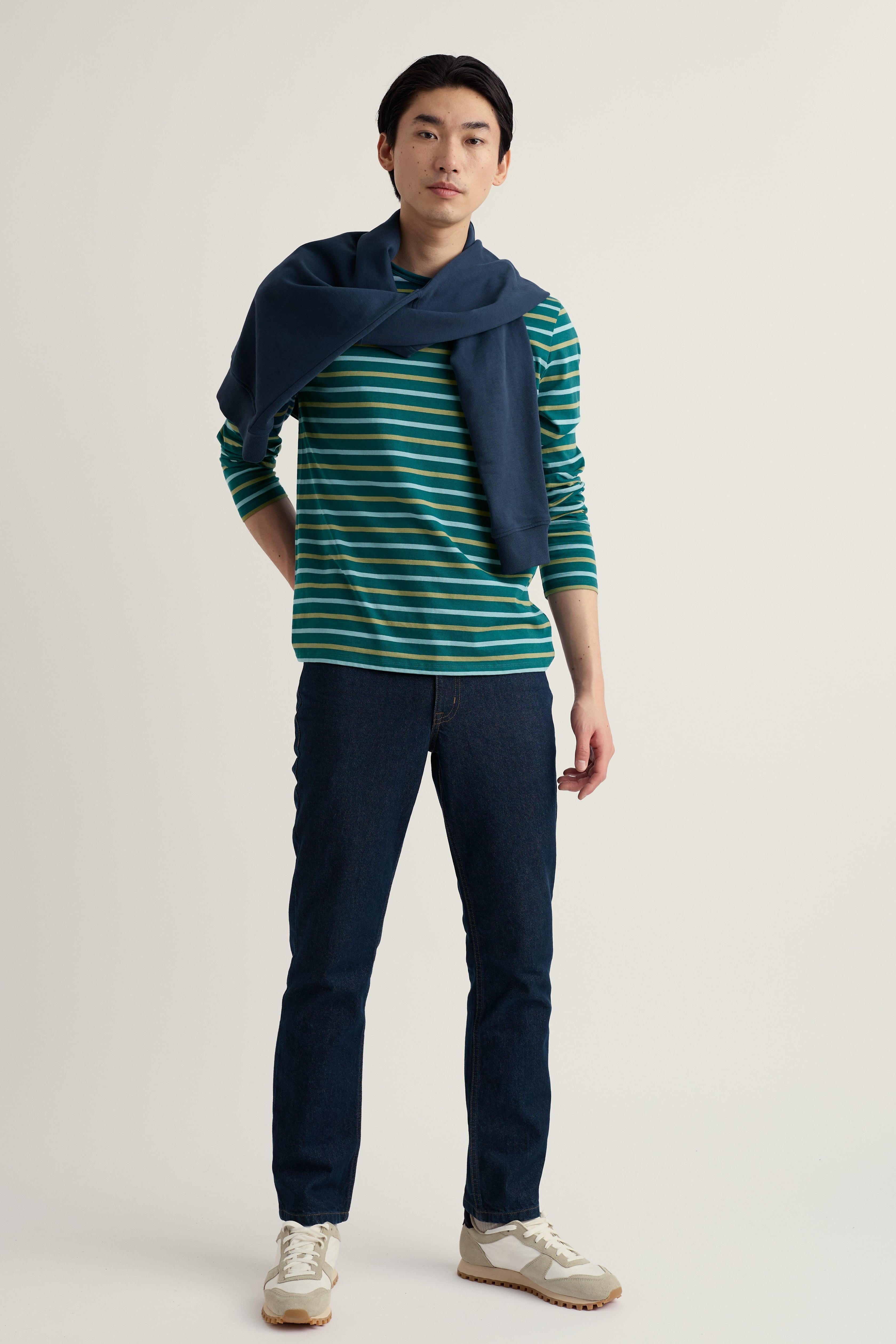 Man wearing a striped organic cotton top and navy pants with a blue scarf on a plain background