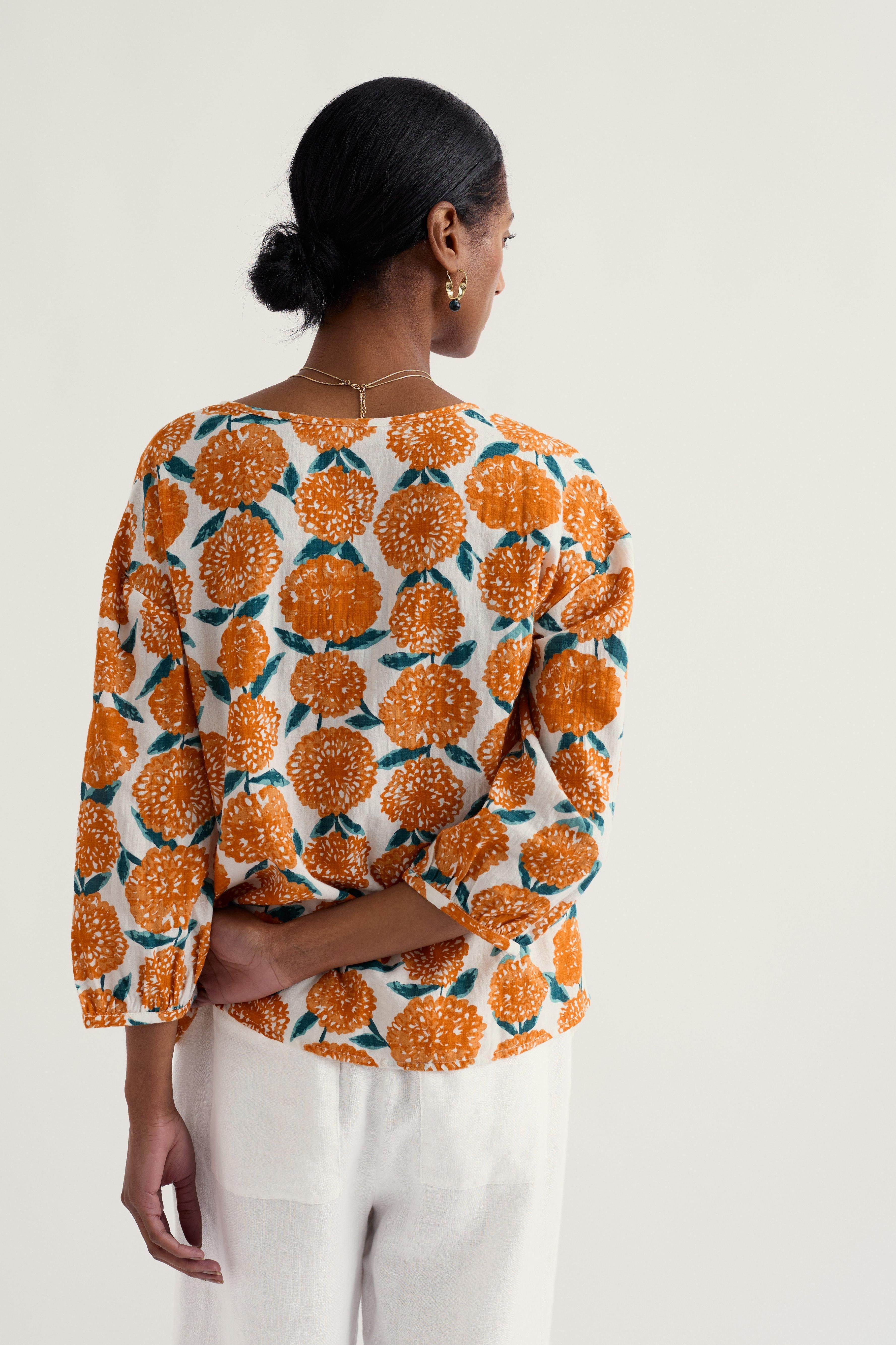 Woman wearing a patterned organic cotton blouse with orange and white design on a plain background