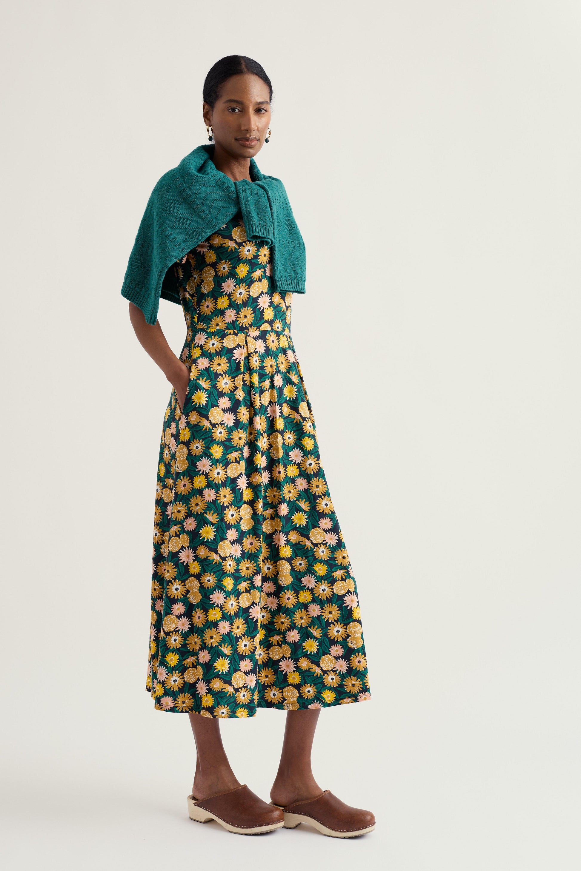 Woman wearing a floral organic cotton dress with a green shawl on a white background