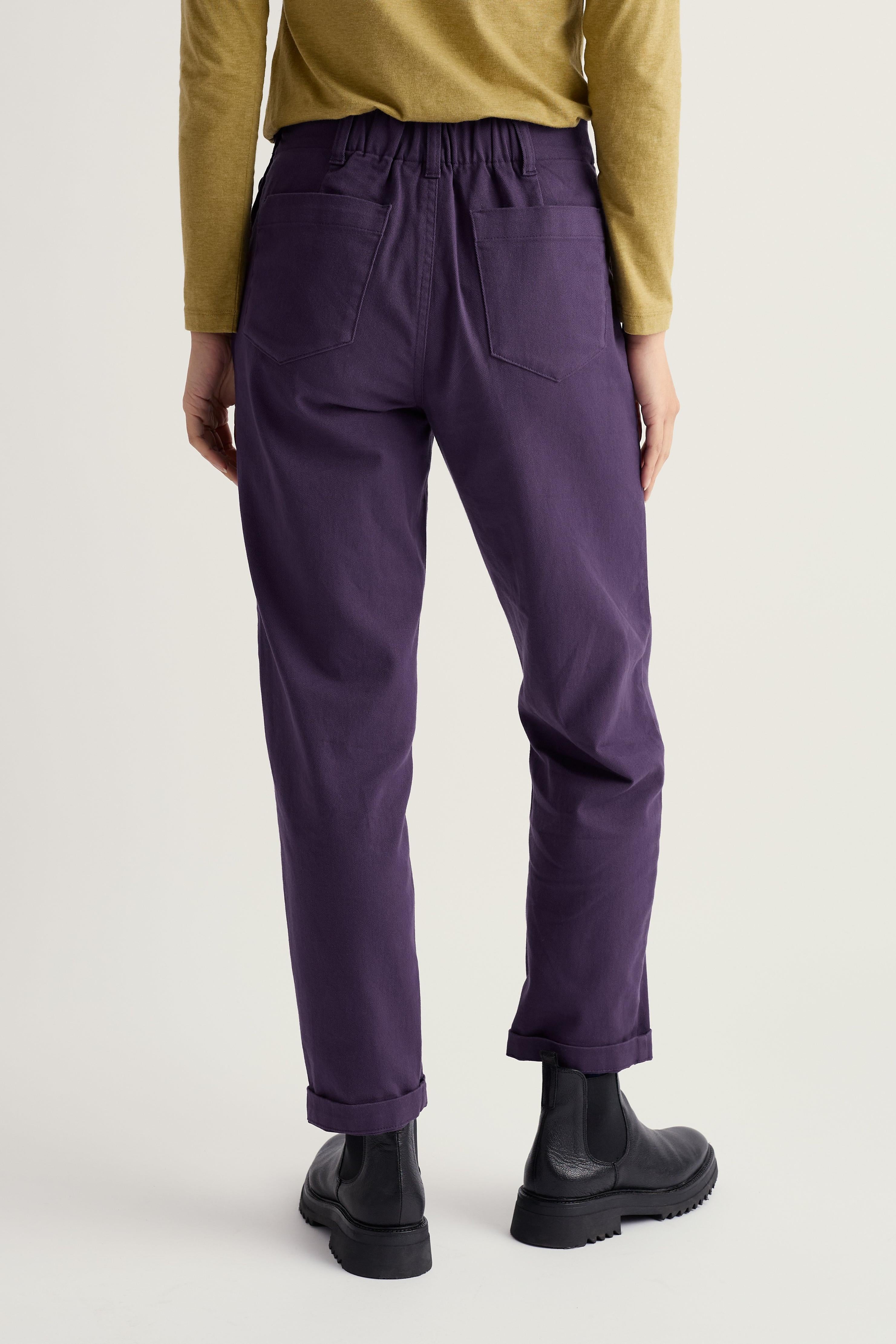 Person wearing purple organic cotton pants and black boots on a plain background