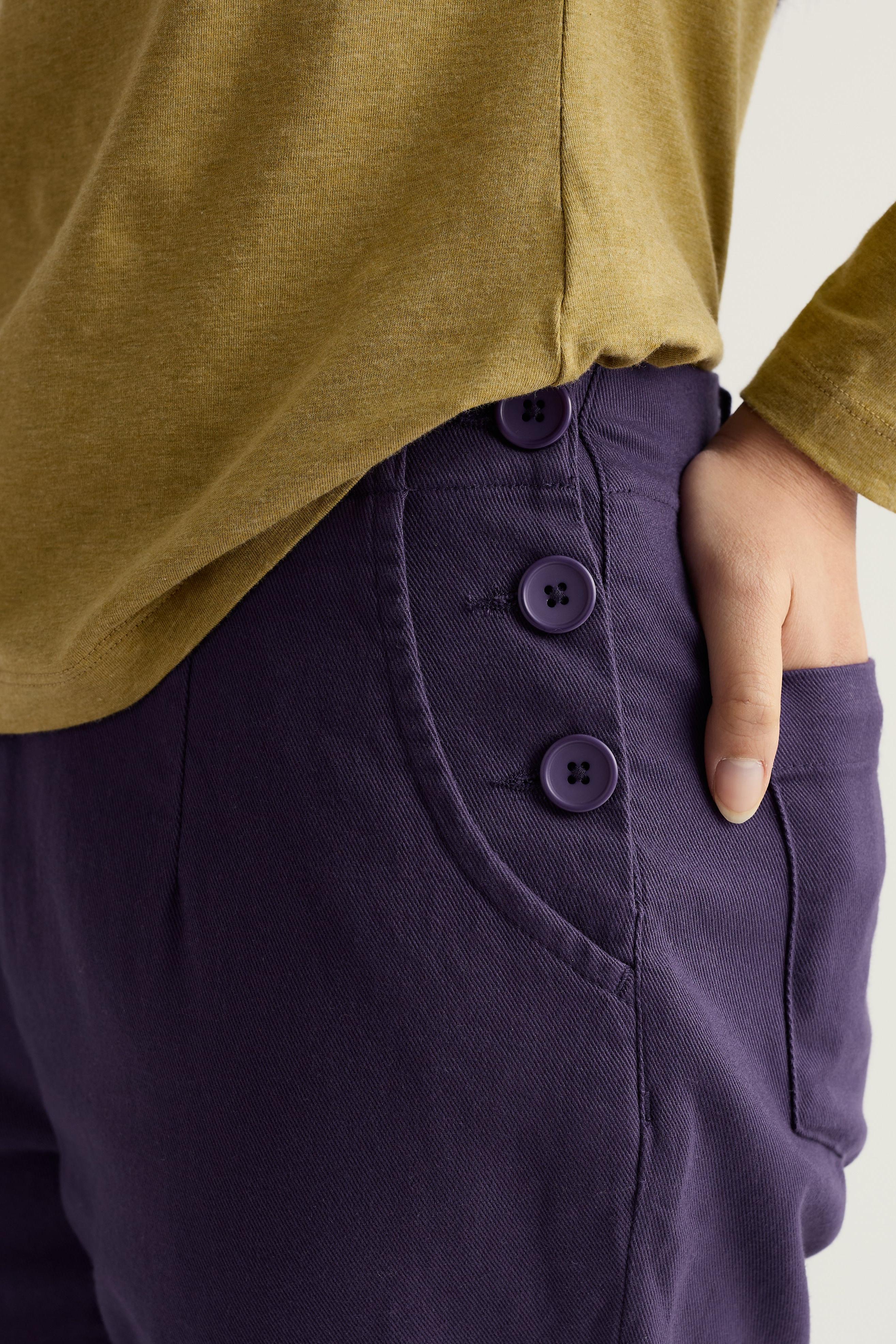Purple organic cotton pants with button details worn by a model, paired with a mustard yellow top.