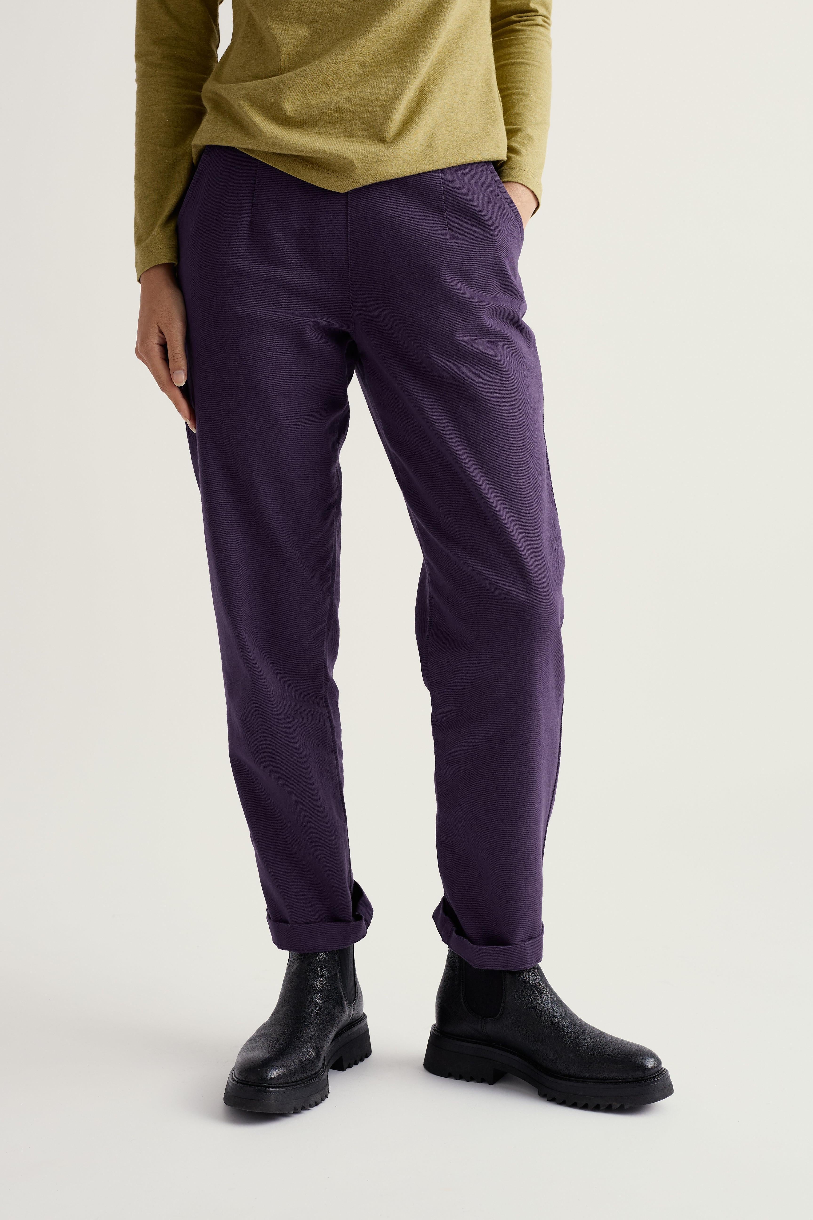Person wearing purple tapered pants and black shoes on a white background