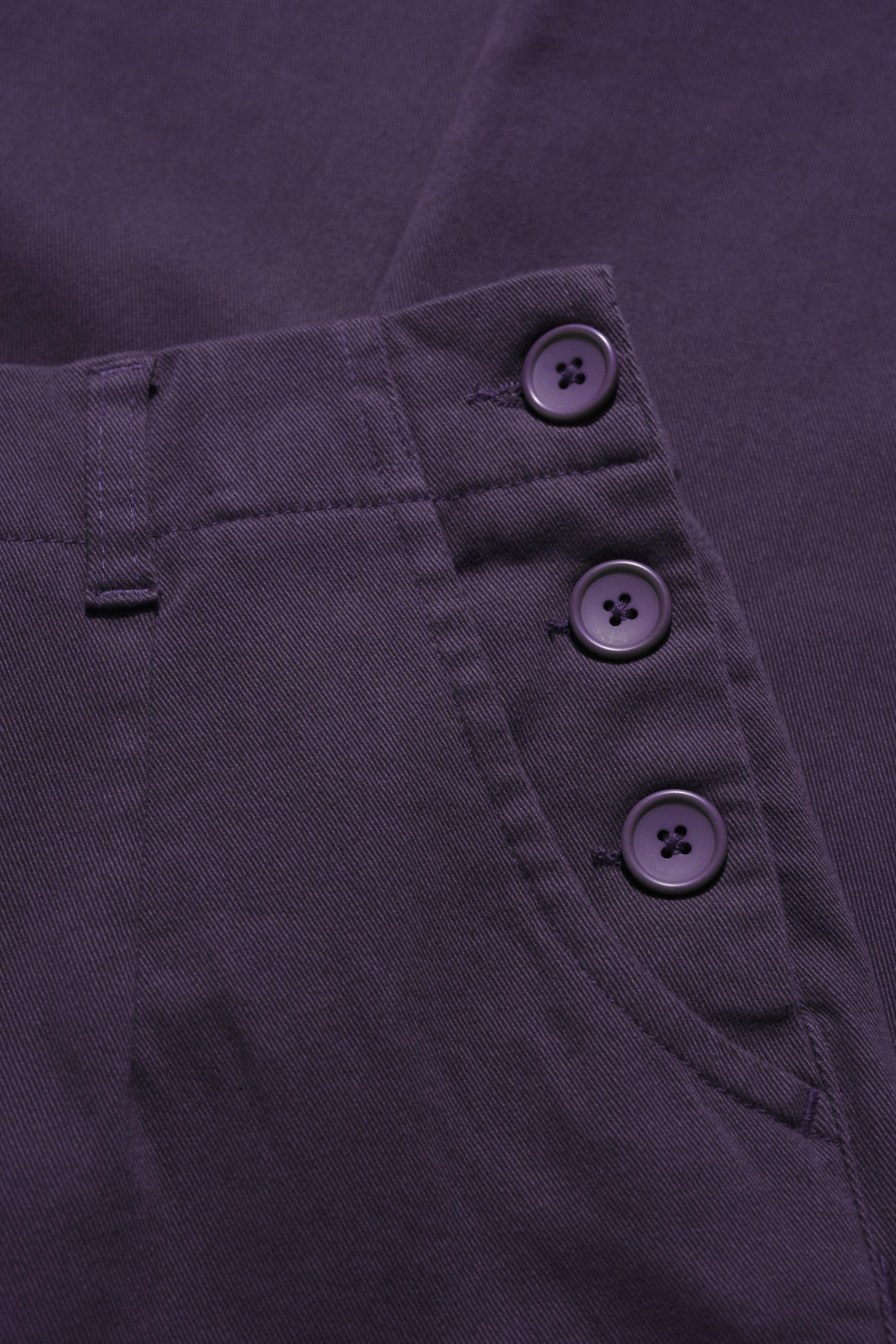 Close-up of a purple trousers with buttons on a matching fabric background