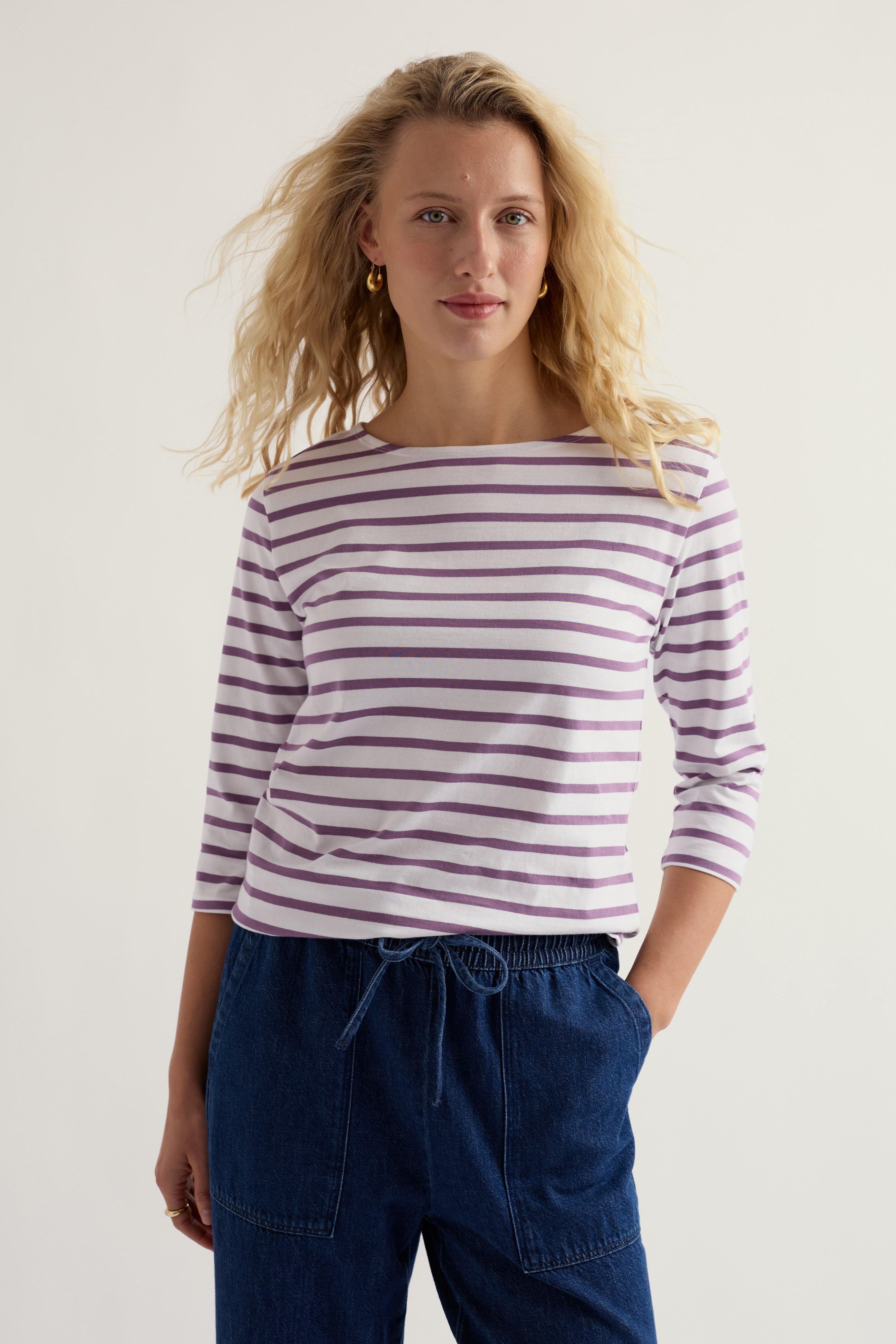 Woman wearing a striped long-sleeve shirt and blue pants against a plain background