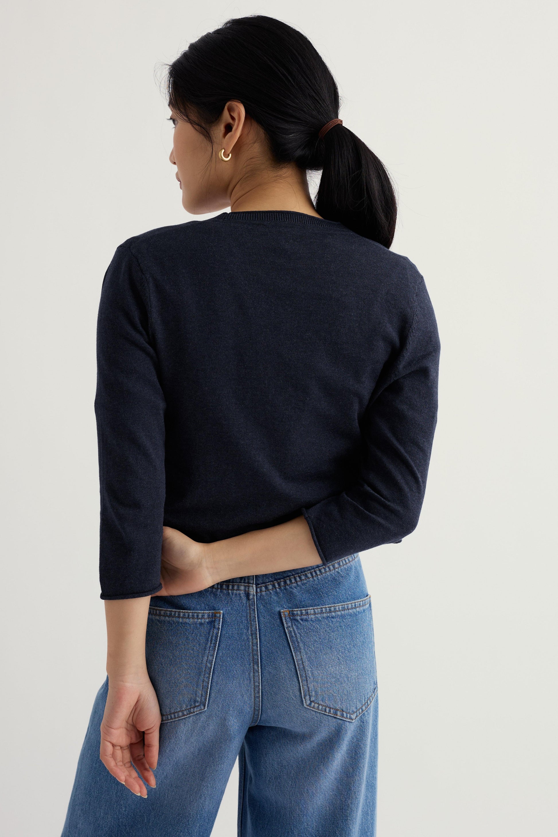 Model wearing a navy organic cotton cardigan and blue jeans on a plain background