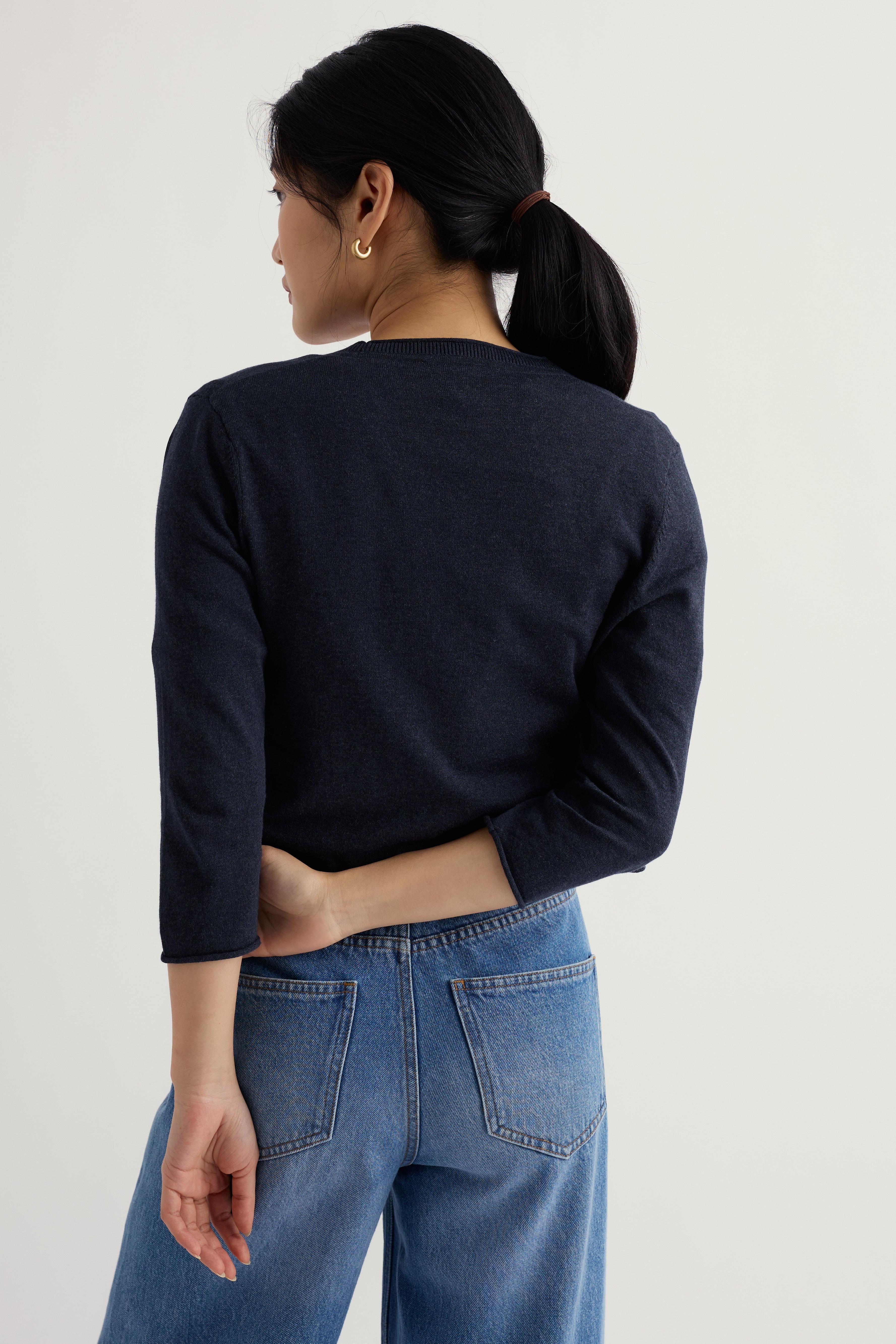 Model wearing a navy organic cotton cardigan and blue jeans on a plain background