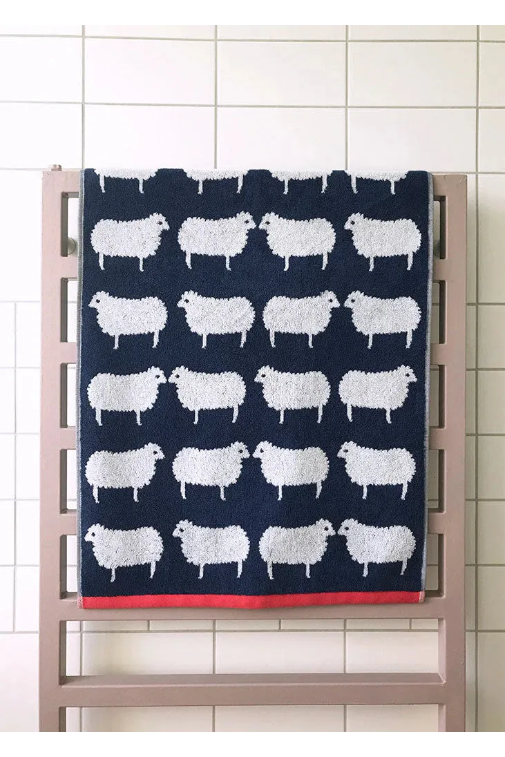 Navy towel with white sheep pattern hanging on a rack against a tiled wall.