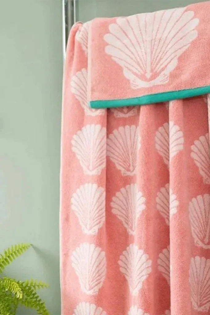Pink towel with white shell pattern draped over a green rack against a light green wall.