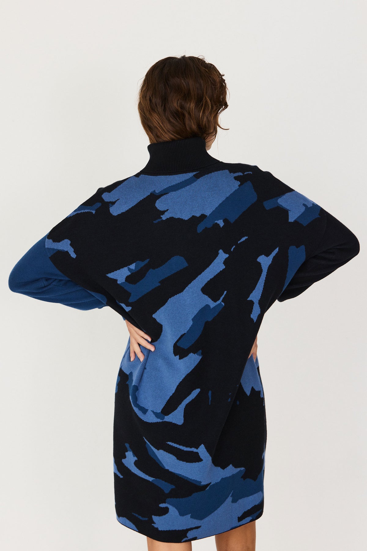 Rear view of a woman wearing a black and blue patterned cotton knit dress with a turtleneck.