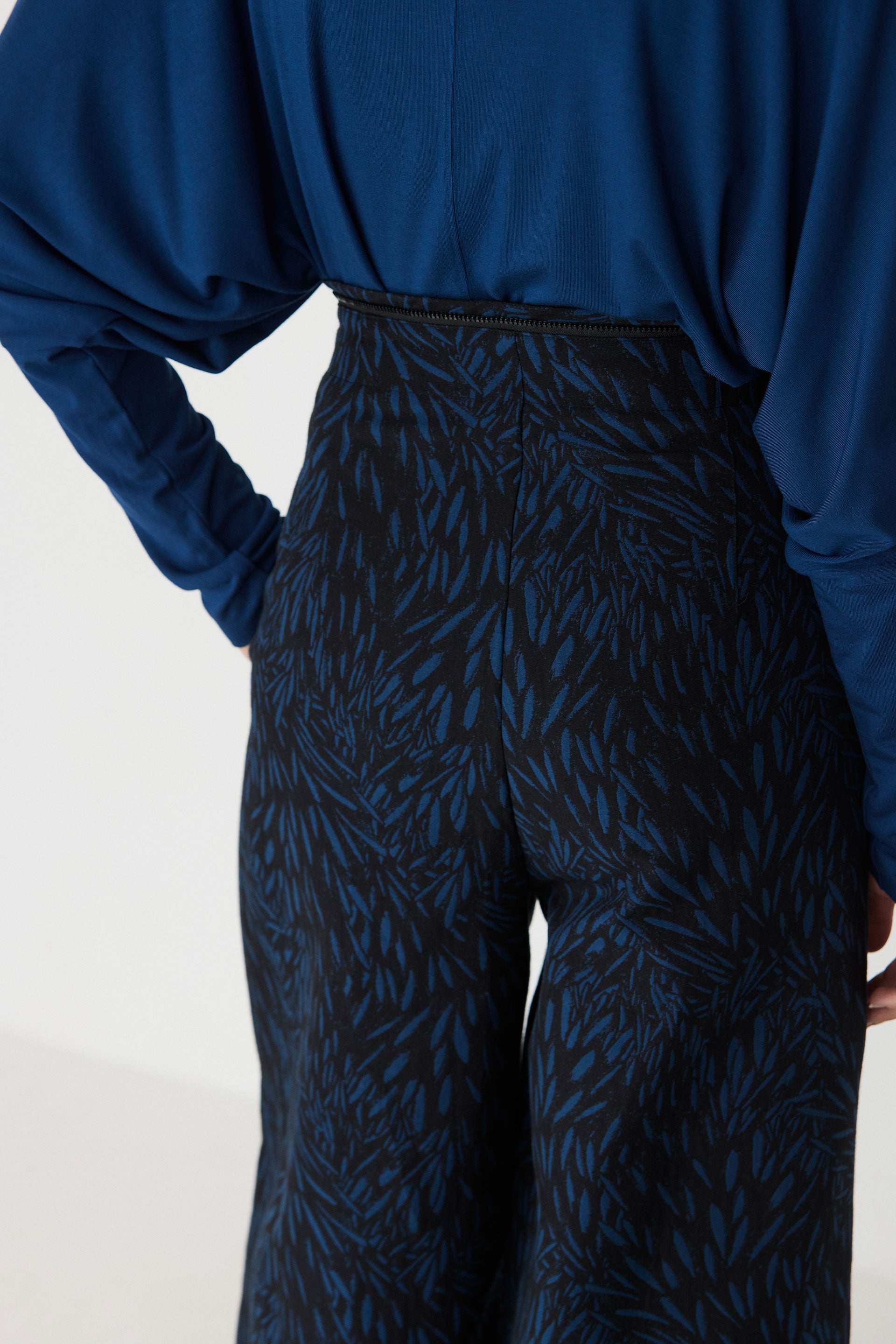 Rear view of a model wearing a blue SKFK detachable jumpsuit with a black and blue leaf pattern.