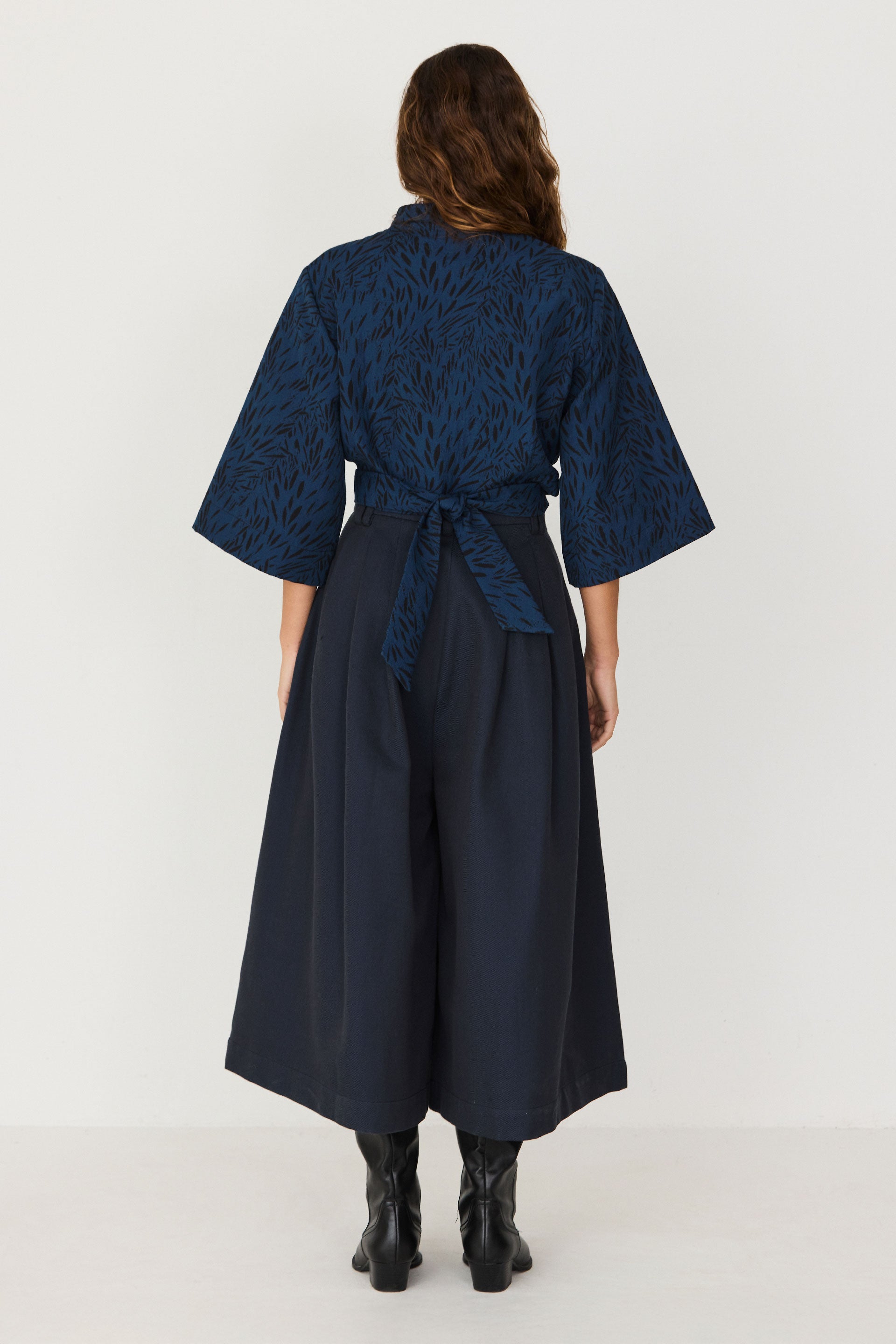 Rear view of a woman wearing a blue patterned sustainable two-piece style jumpsuit with wide legs and a waist tie.