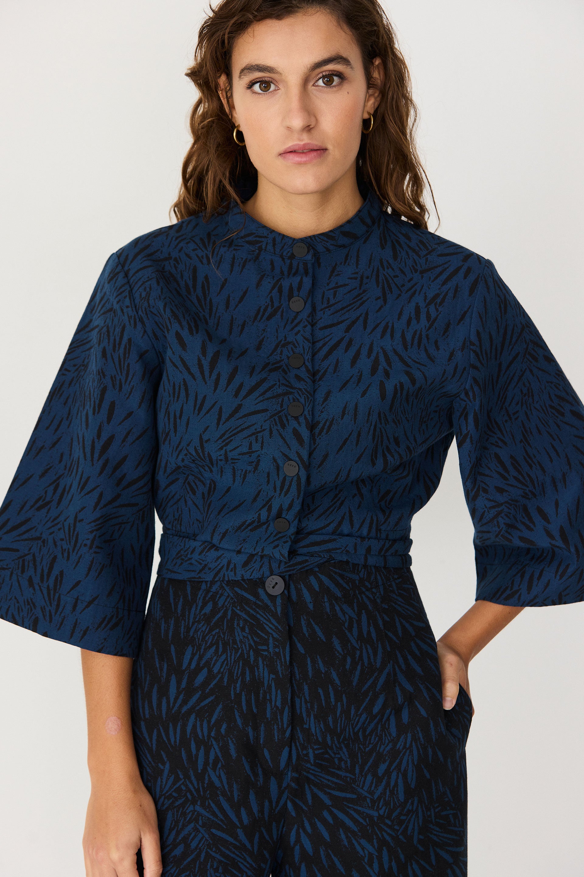 A woman wearing a stylish blue two-piece jumpsuit with patterned top and dark trousers.
