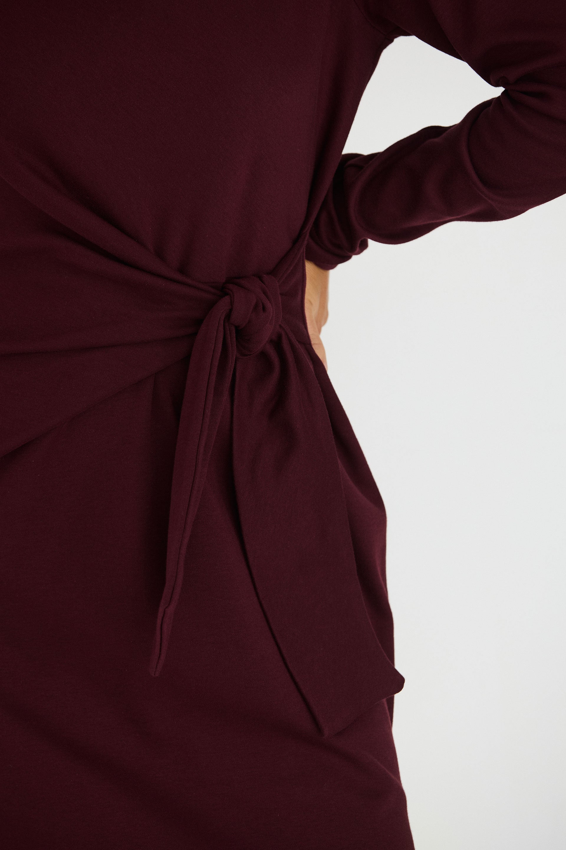 Close up of a chocolate brown organic cotton midi dress by SKFK featuring a side tie waist detail.