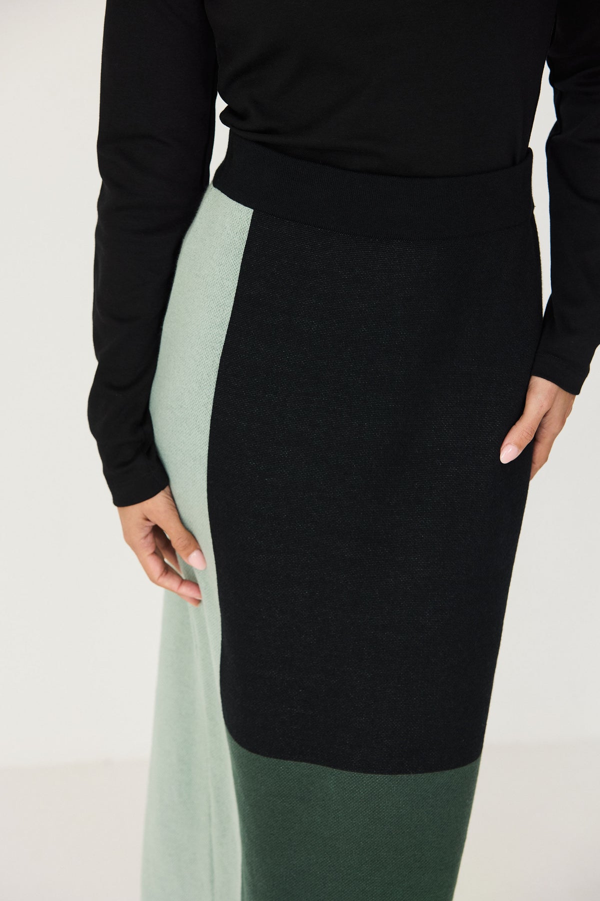 A model wearing a black top and a green and black cotton knit ankle length skirt against a white background.