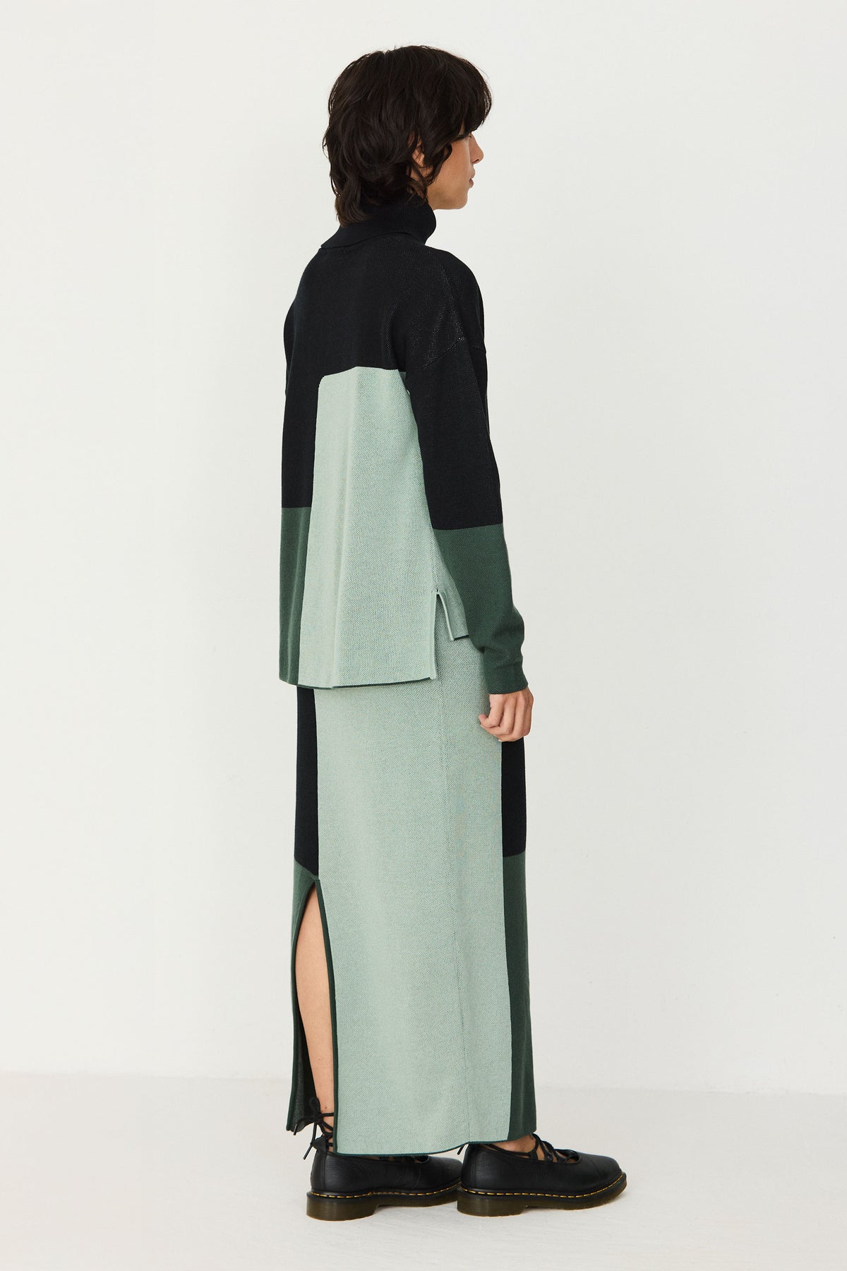 Model wearing a SKFK colourblock green cotton sweater and matching knit skirt against a white studio background.