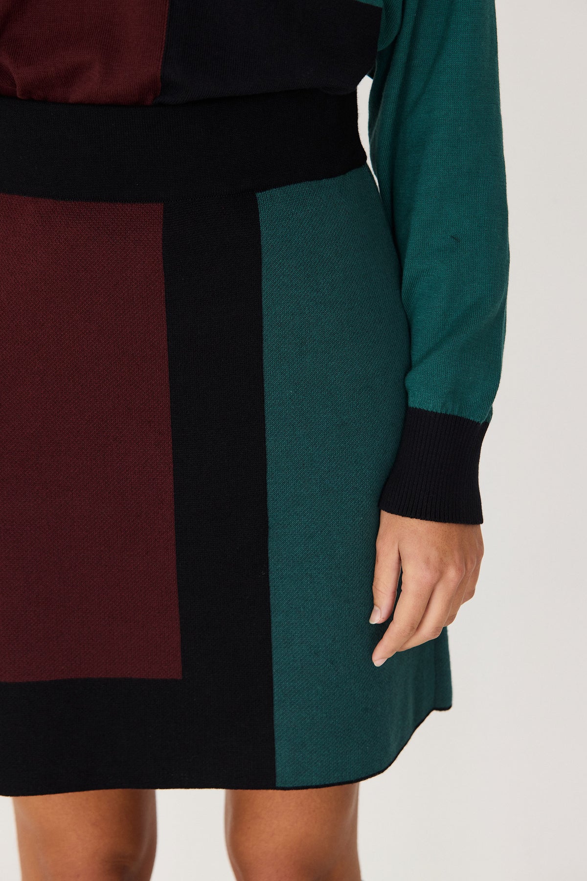 Close-up of a person wearing a colorblock SKFK winter skirt coord outfit in dark green, burgundy, and black.