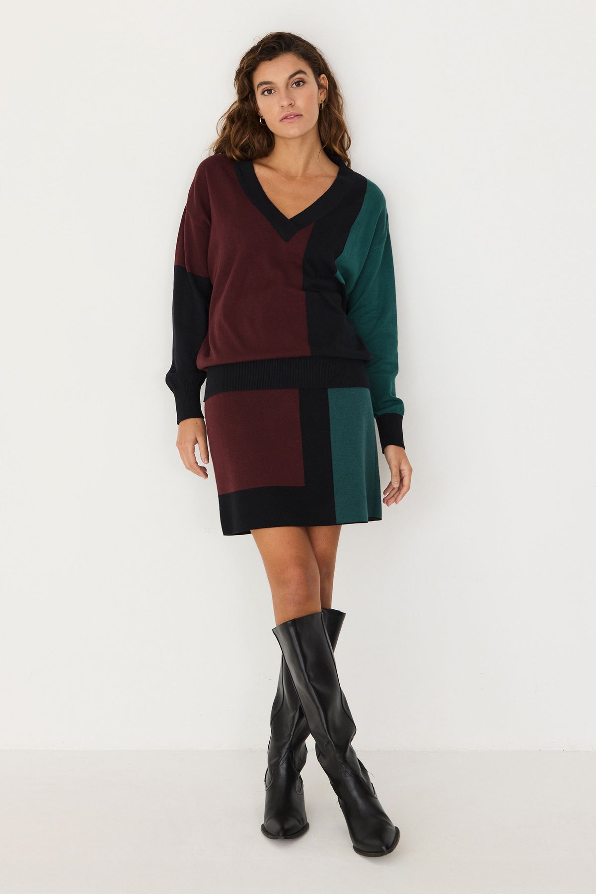 A woman posing in a colour-blocked cotton knitwear coord set with a v-neck jumper and skirt.