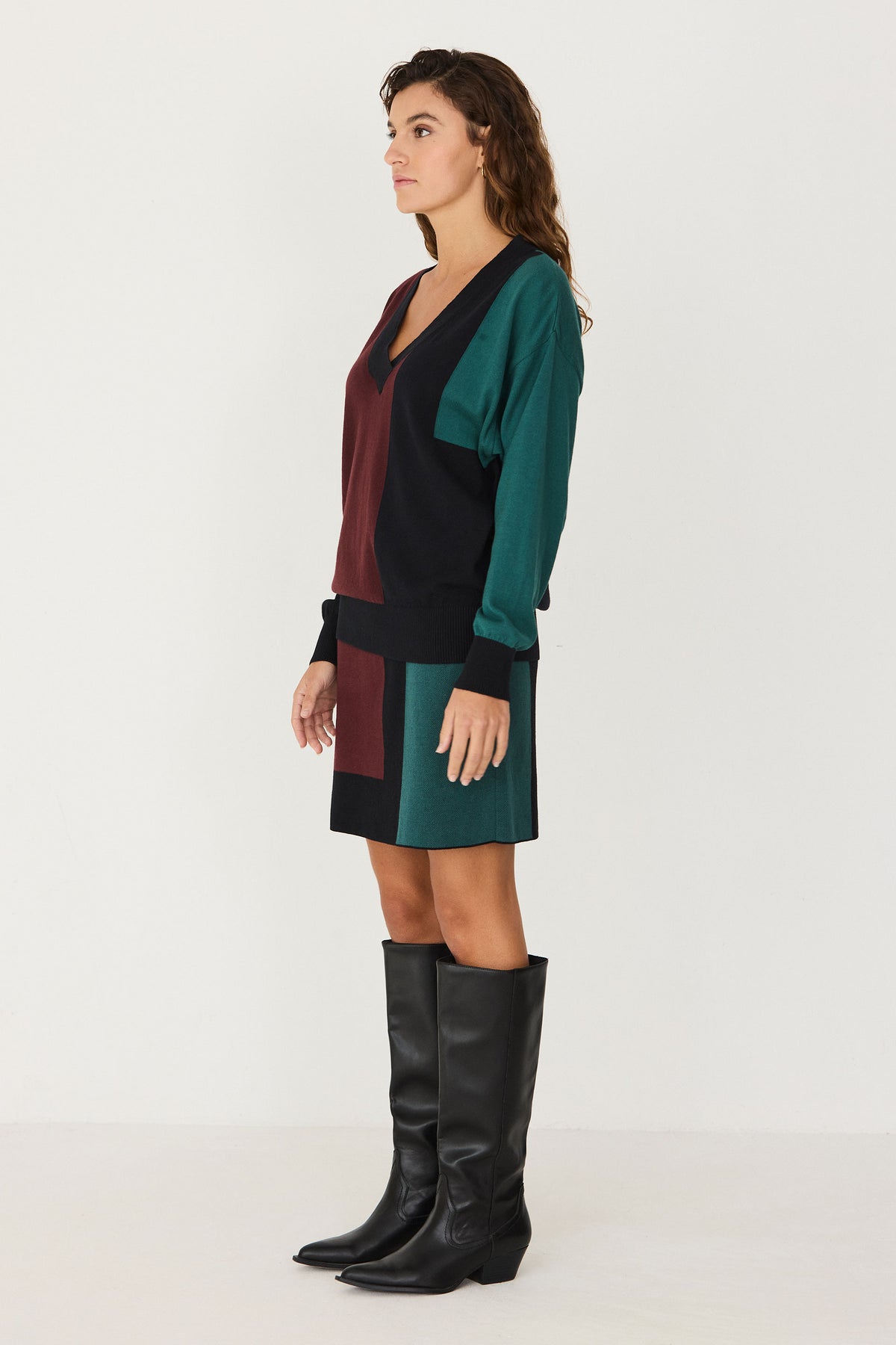 A woman wearing a colourful cotton knitwear jumper and matching skirt coord set against a white background.
