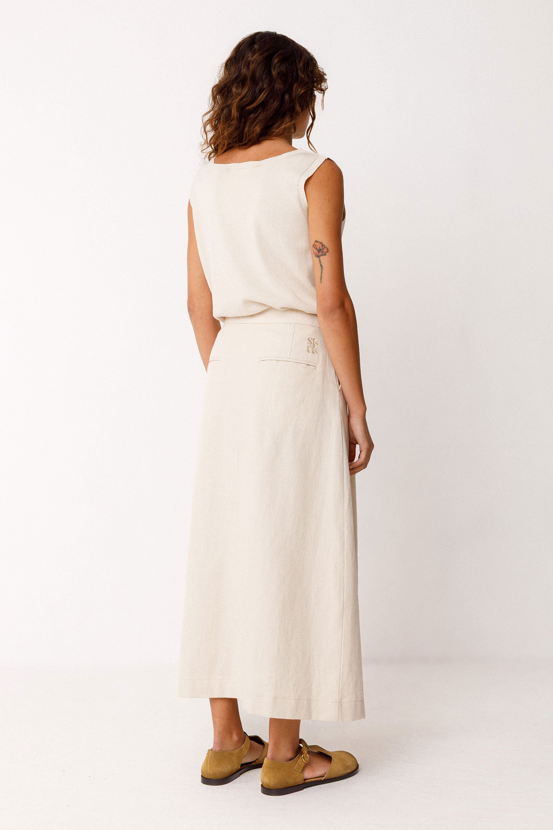 Woman wearing an ivory midi skirt with ivory sleeveless top on a white background