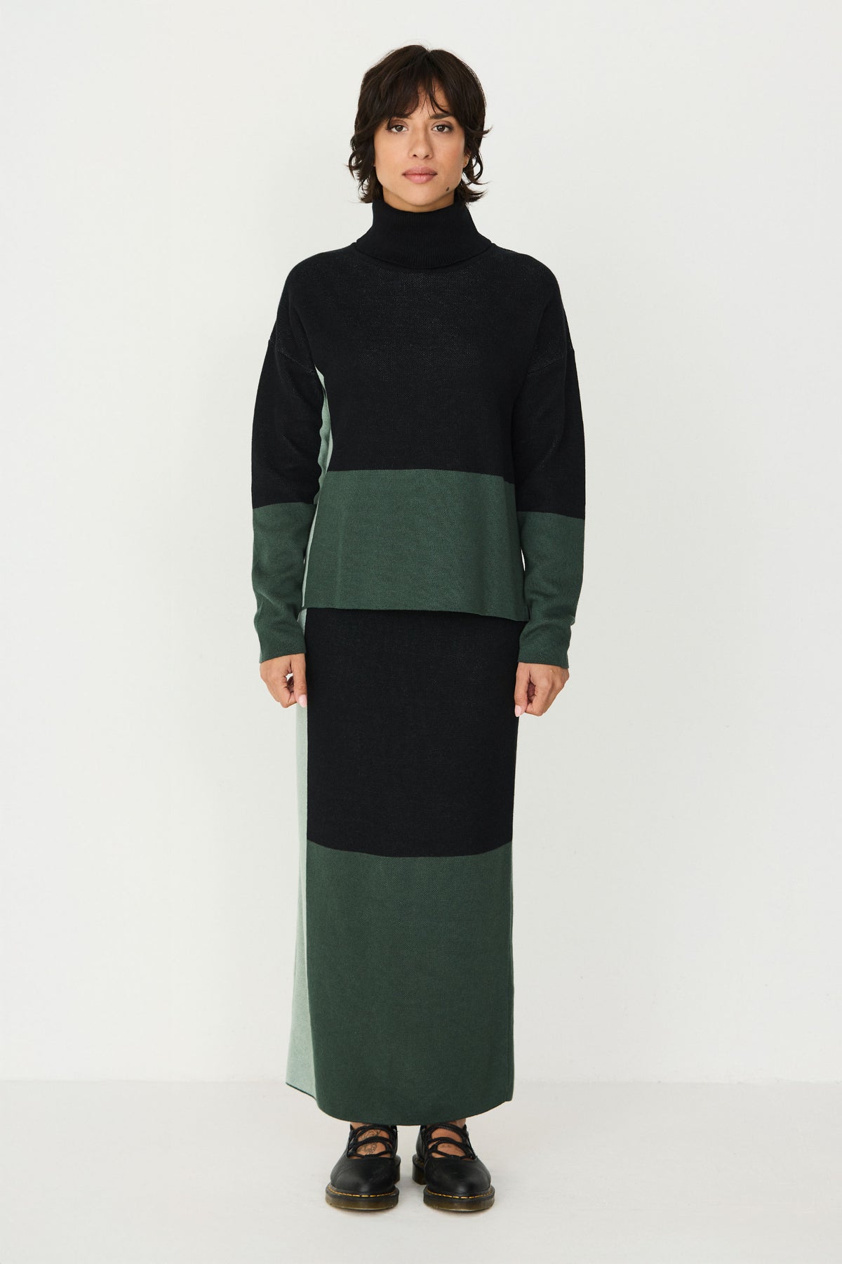 A woman from the back wearing a colour-blocked green cotton sweater and matching knit skirt against a white background.