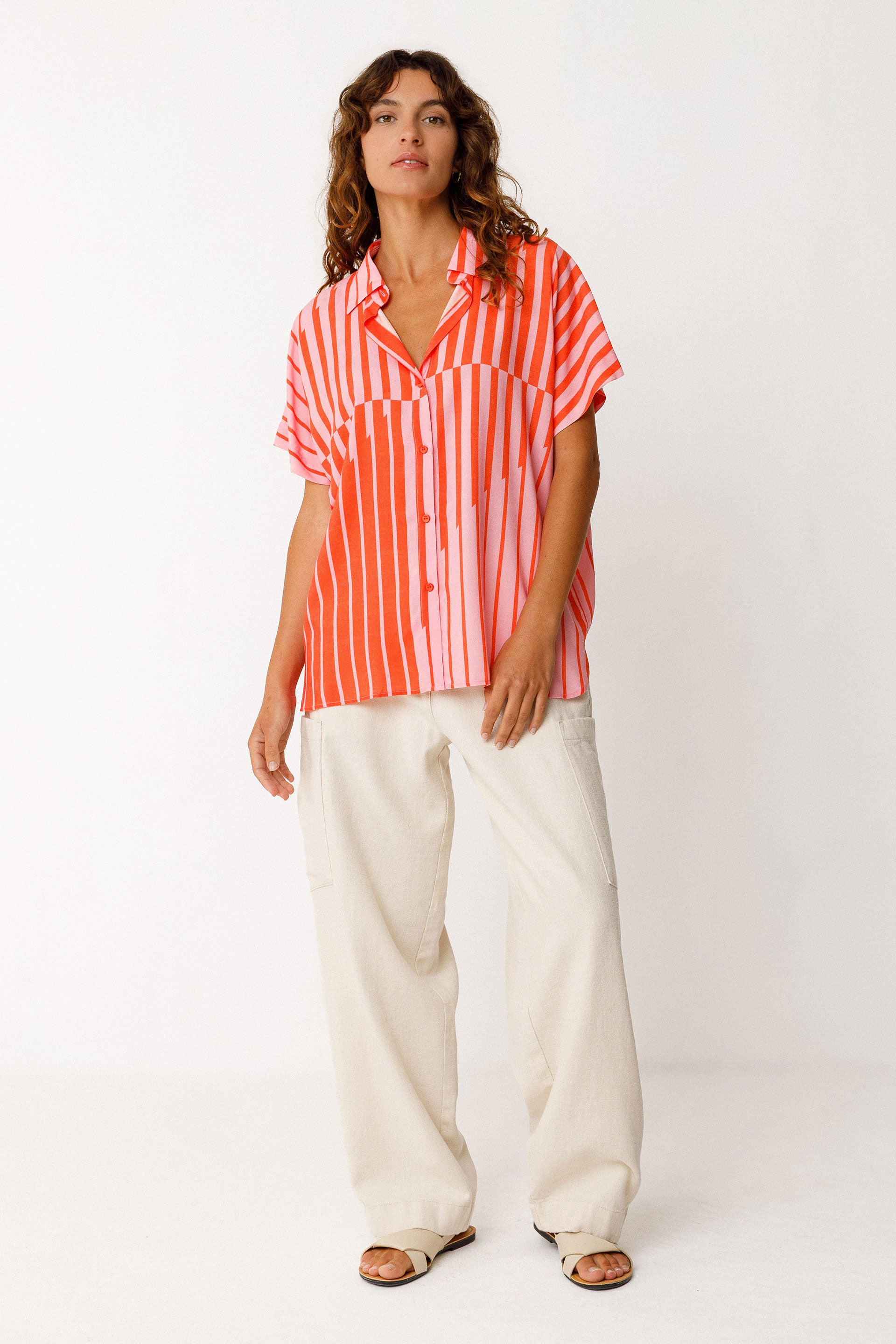 Woman wearing a red and pink striped shirt with white pants on a white background