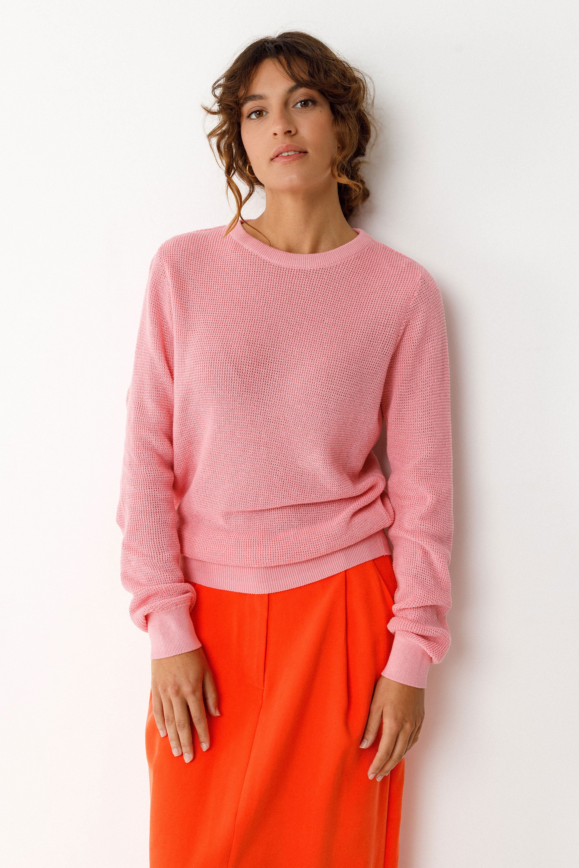 Woman wearing a pink GOTS organic cotton sweater and orange pants against a white background