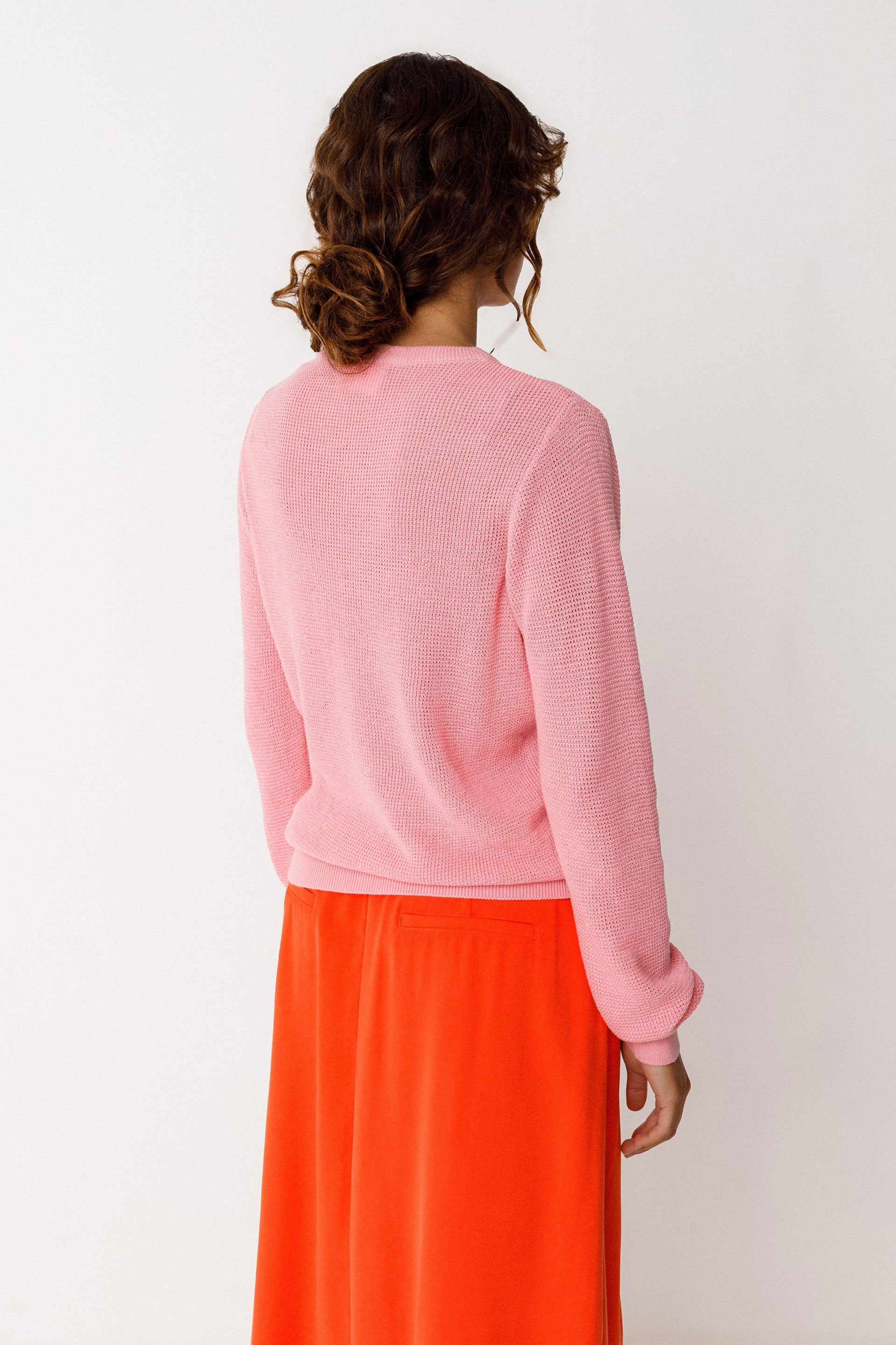 Model wearing a pink organic cotton knit sweater and orange skirt on a white background