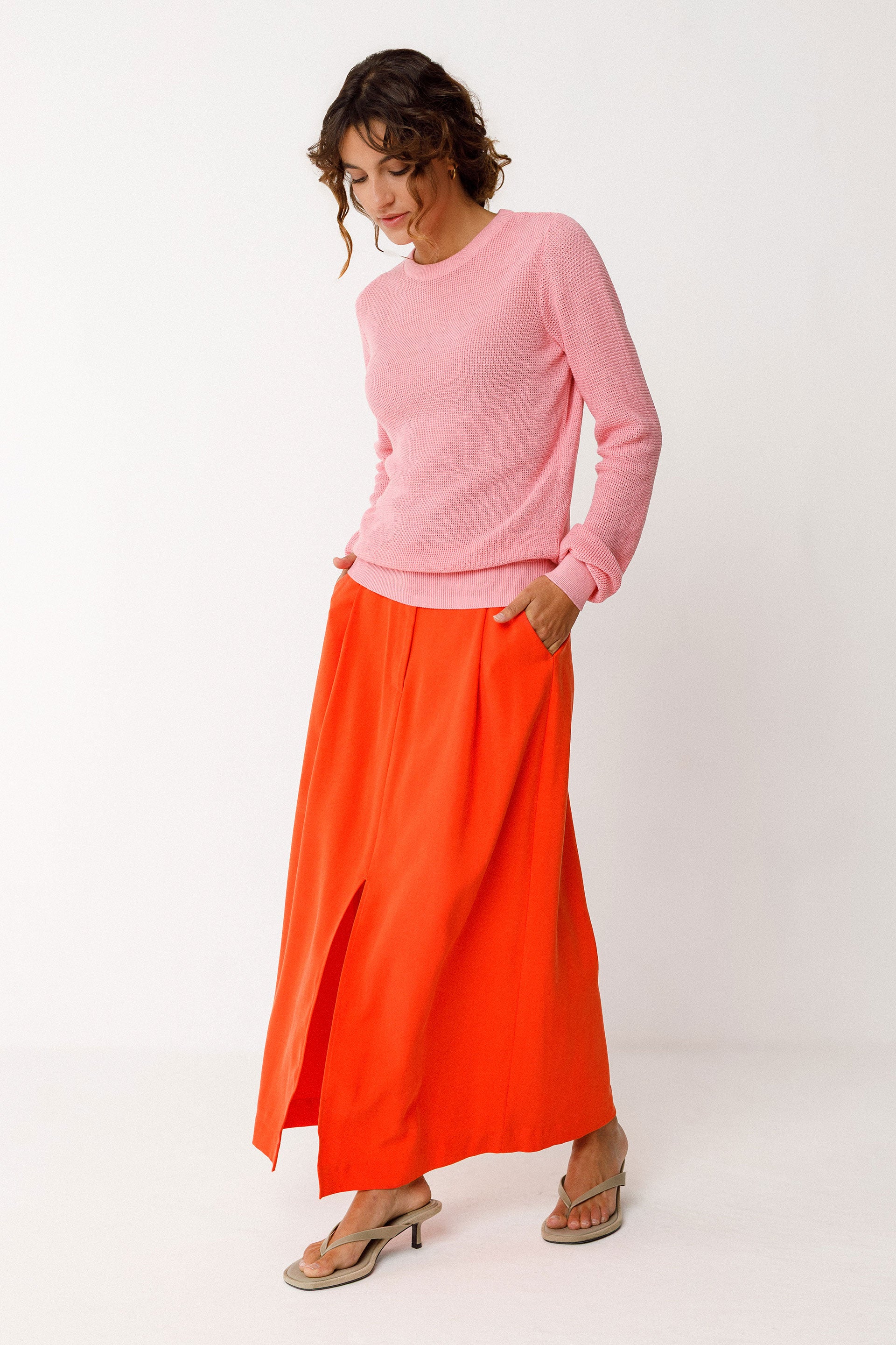 Woman wearing a pink organic cotton knit sweater and orange skirt on a white background