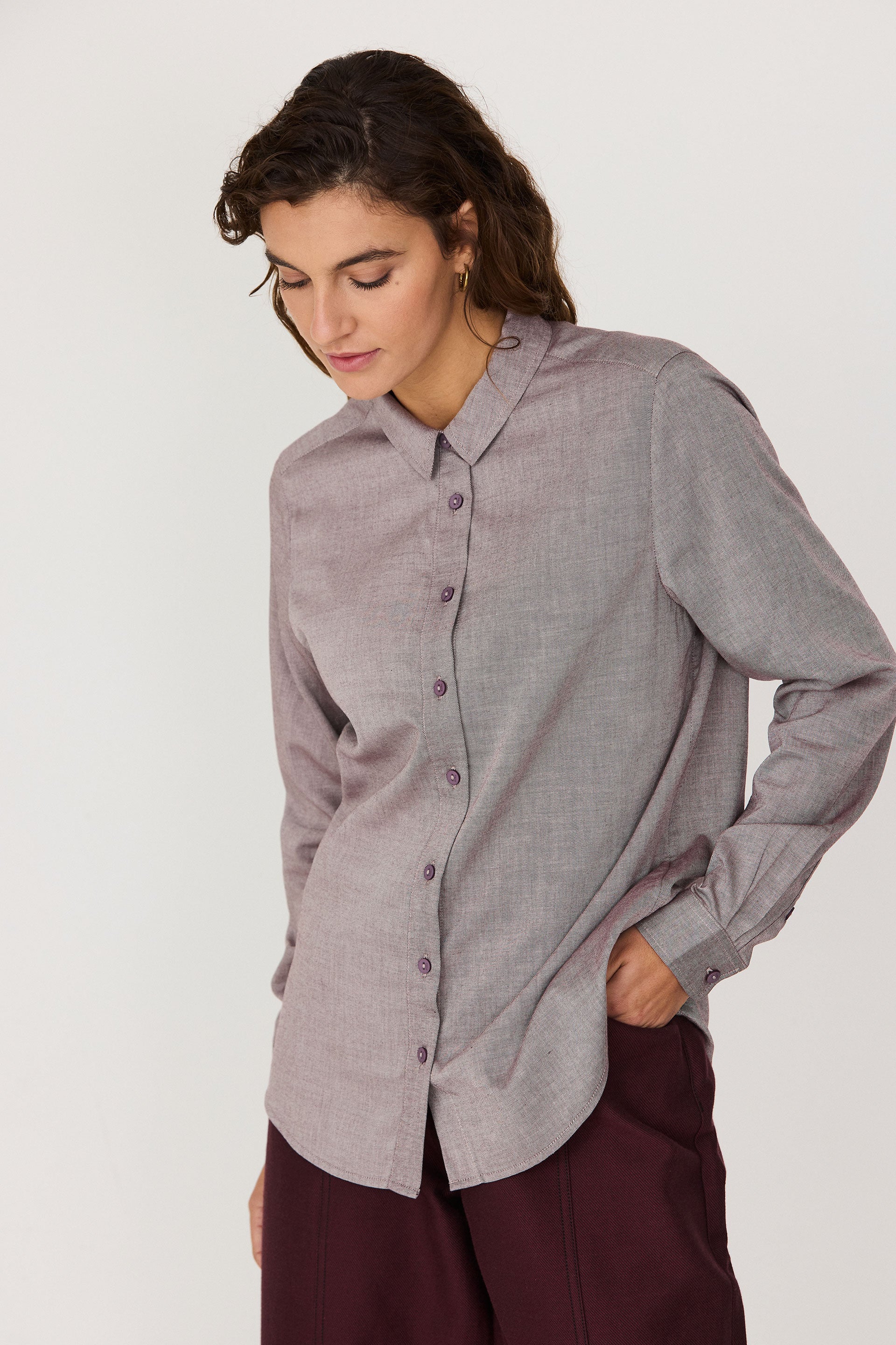 A woman wearing a red melange button-up shirt standing against a plain white background.