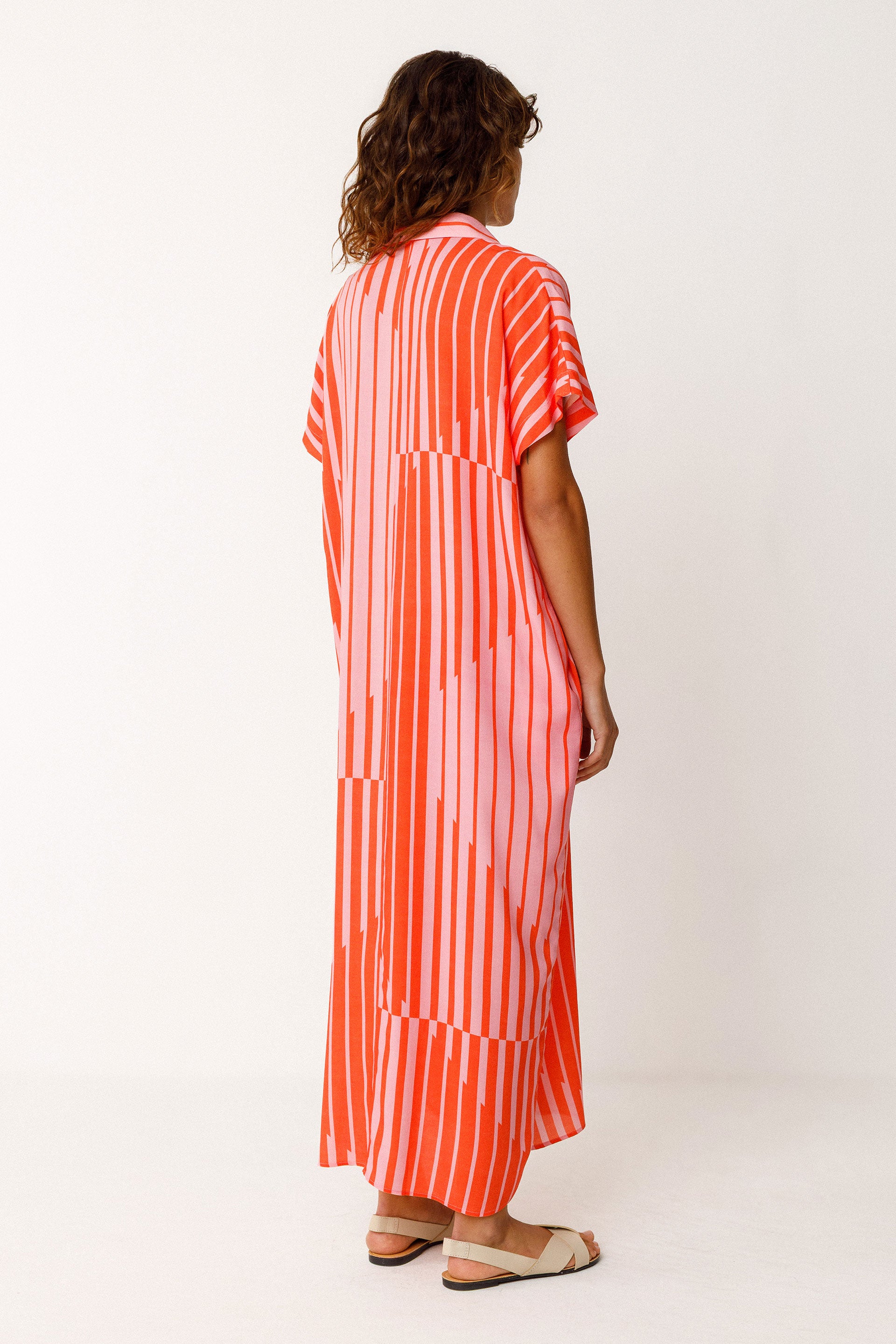 Woman wearing a red and pink striped loose fit dress on a white background