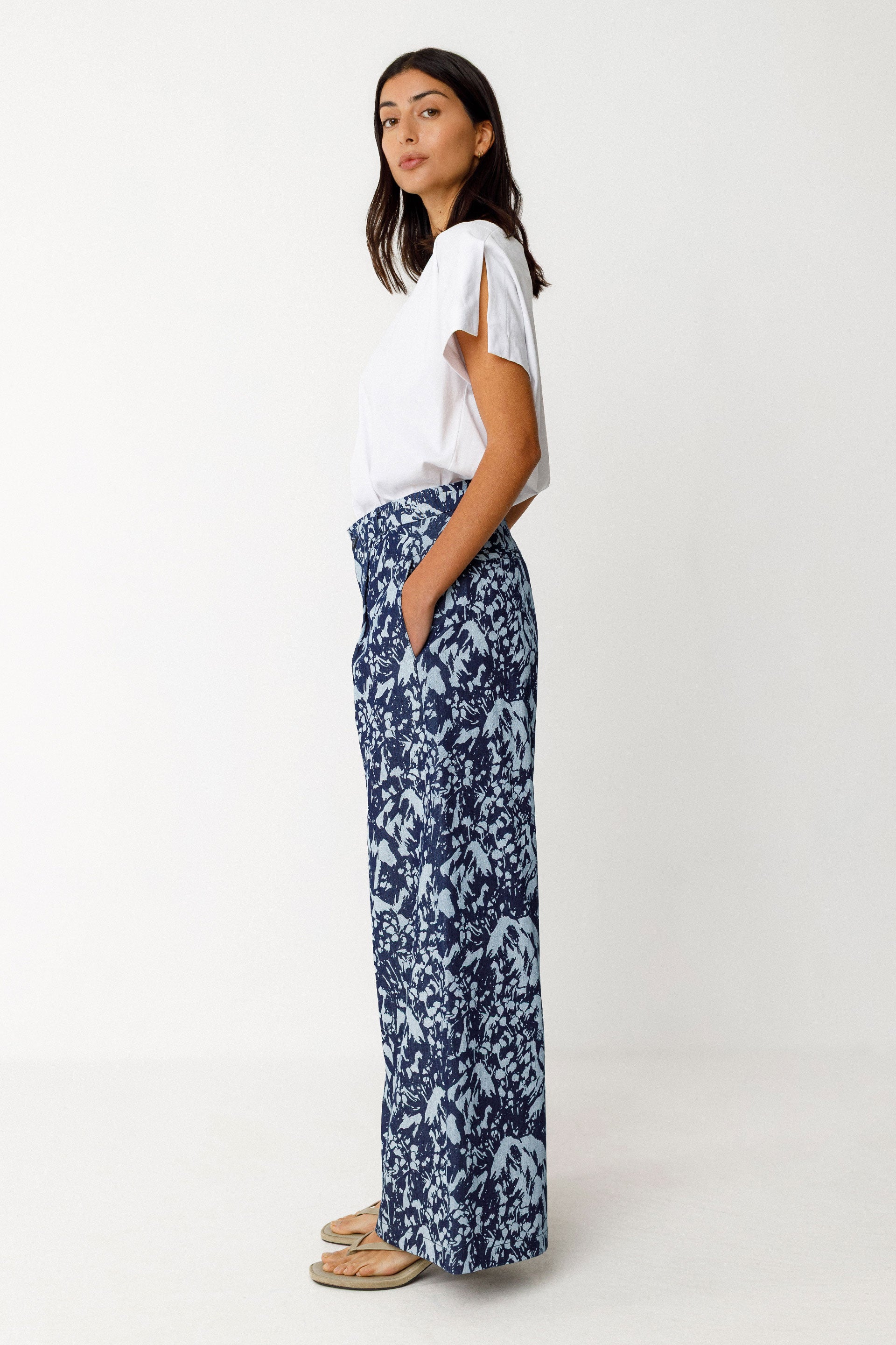 Woman wearing a white top and blue floral SKFK pants on a white background