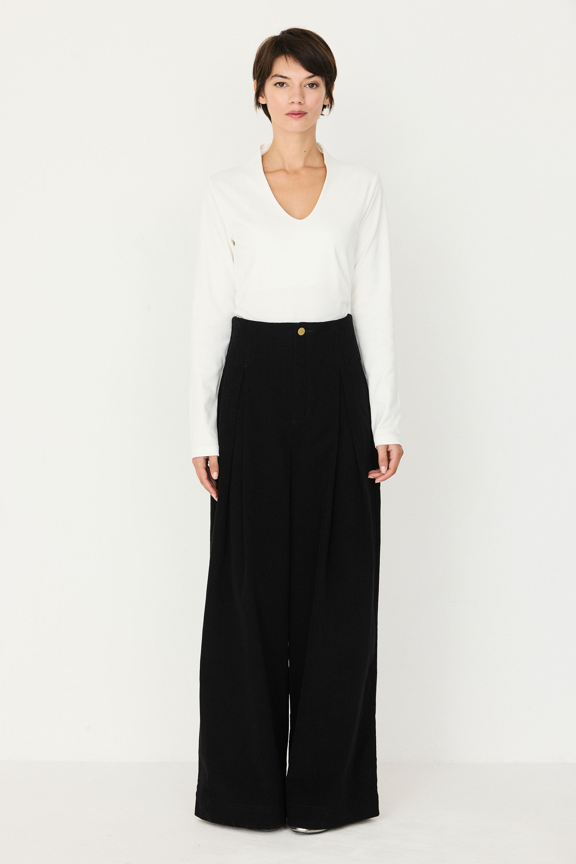 A woman wearing a white long-sleeve organic cotton top and black wide-leg trousers against a white background.