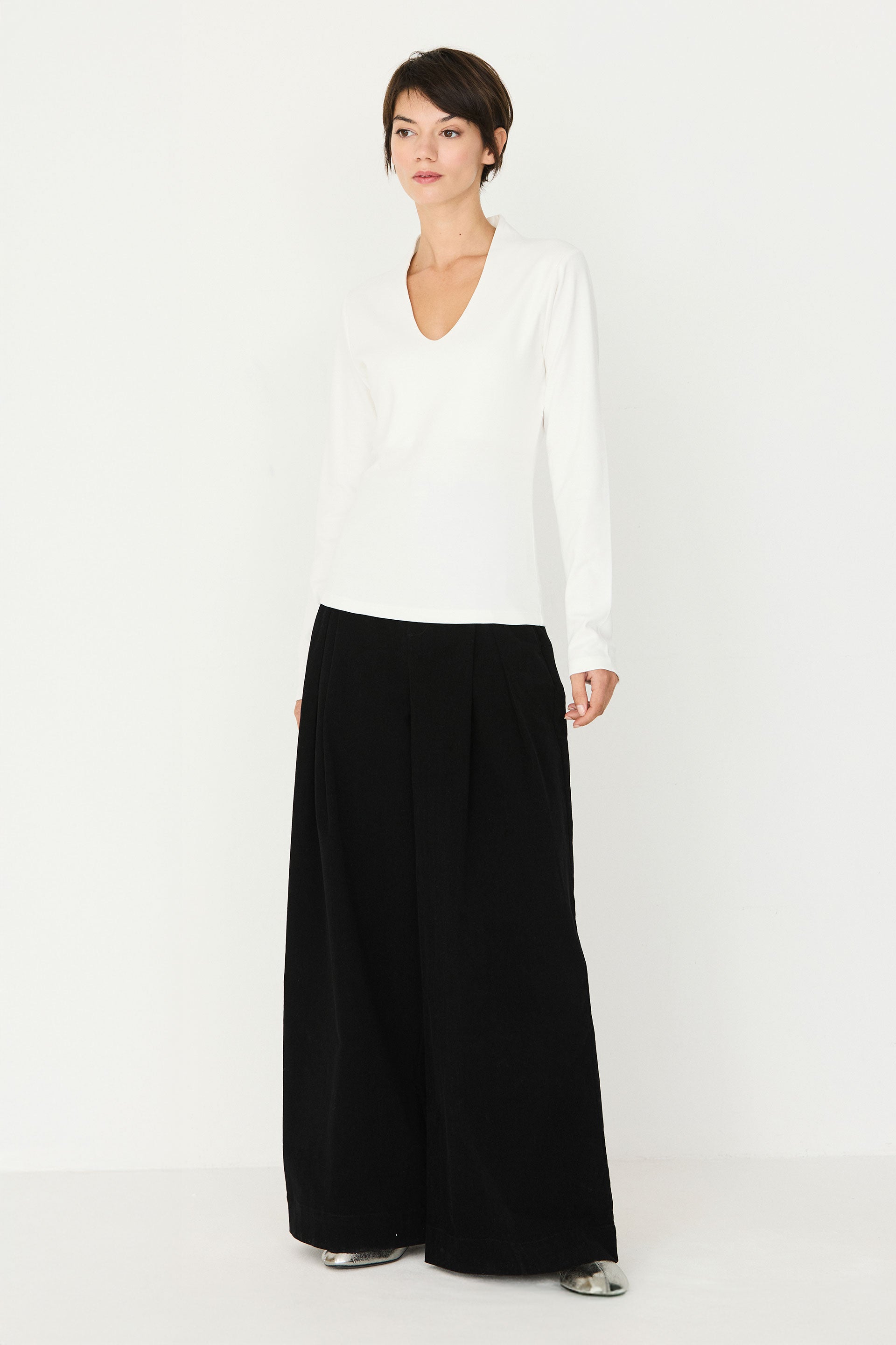 A woman wearing a white long-sleeve organic cotton top with a V-neck, paired with black wide-leg trousers.