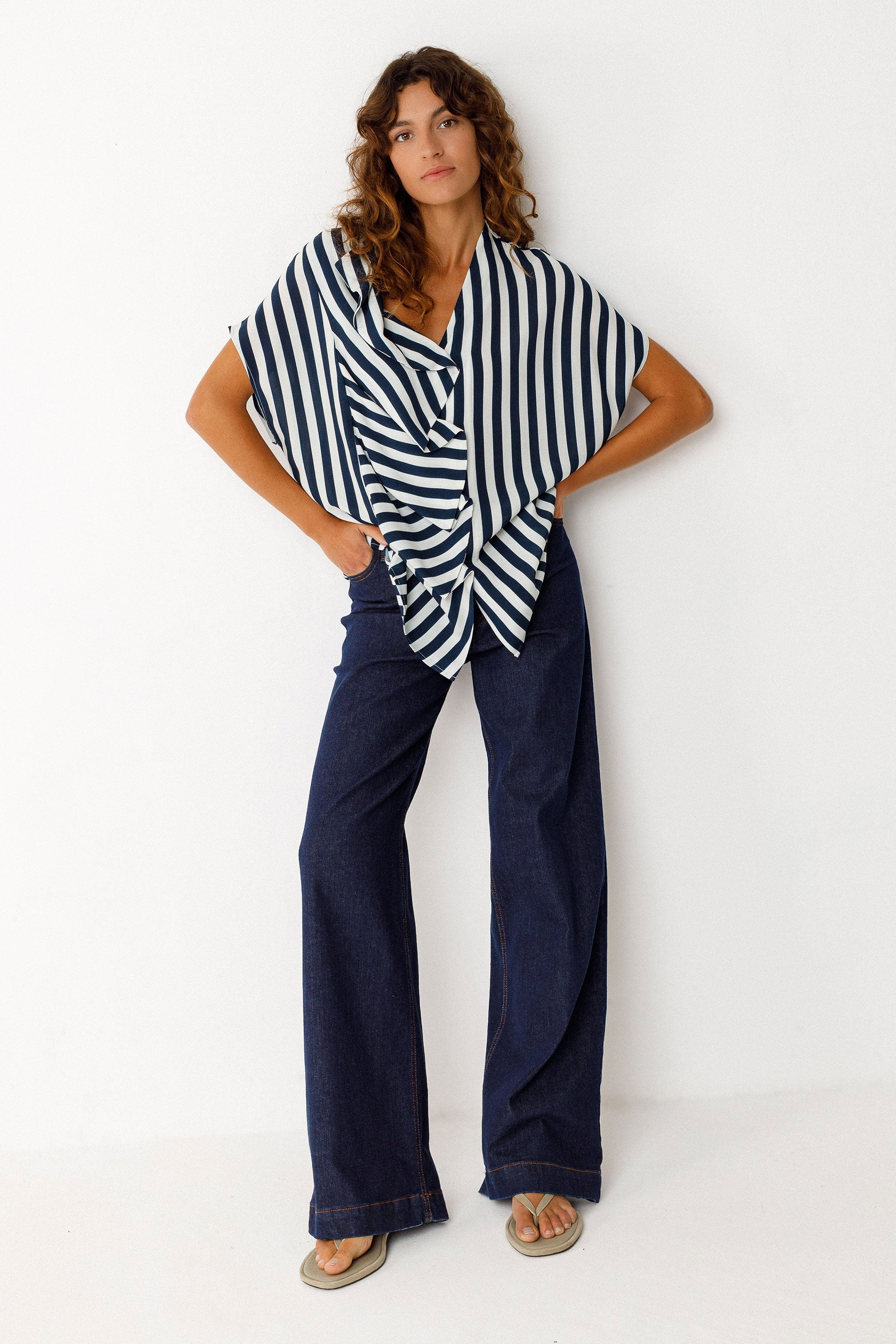 Woman wearing a striped shirt and blue denim jeans against a white background