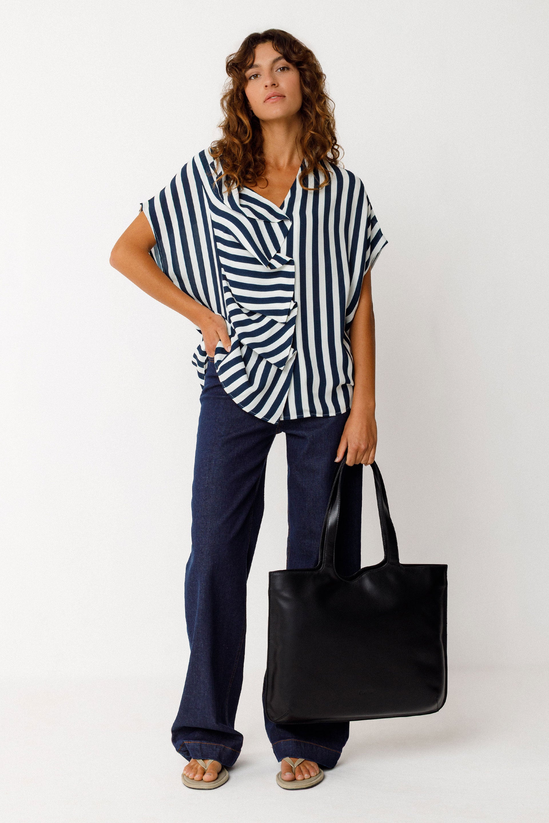 Woman wearing a striped shirt and dark pants, holding a black bag on a white background