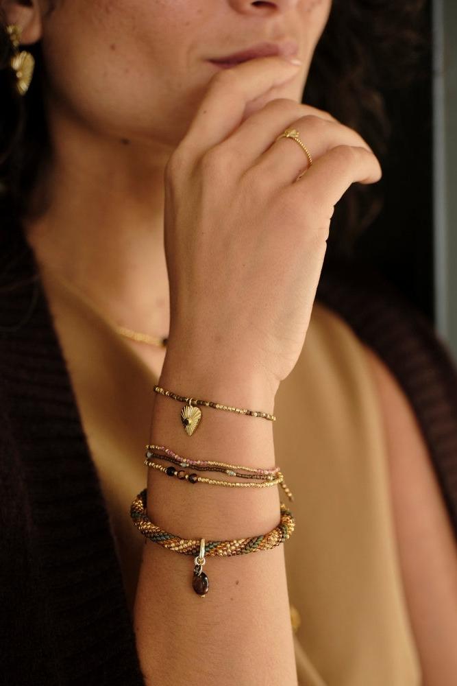 A woman wearing a mix of ethically made bracelets in warm autumn colours. Showing different gemstones including tiger eye