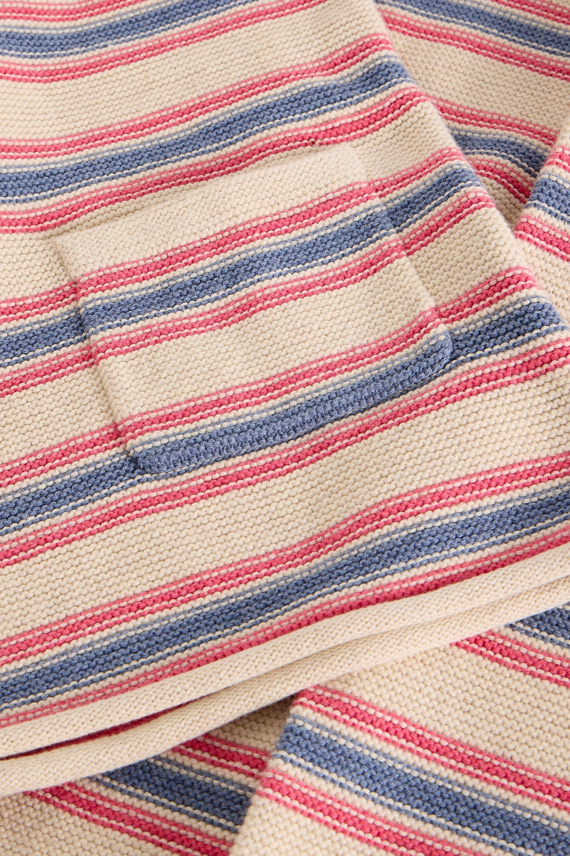 Close-up of a textured fabric with pink and blue stripes on a white base, featuring a sewn pocket.