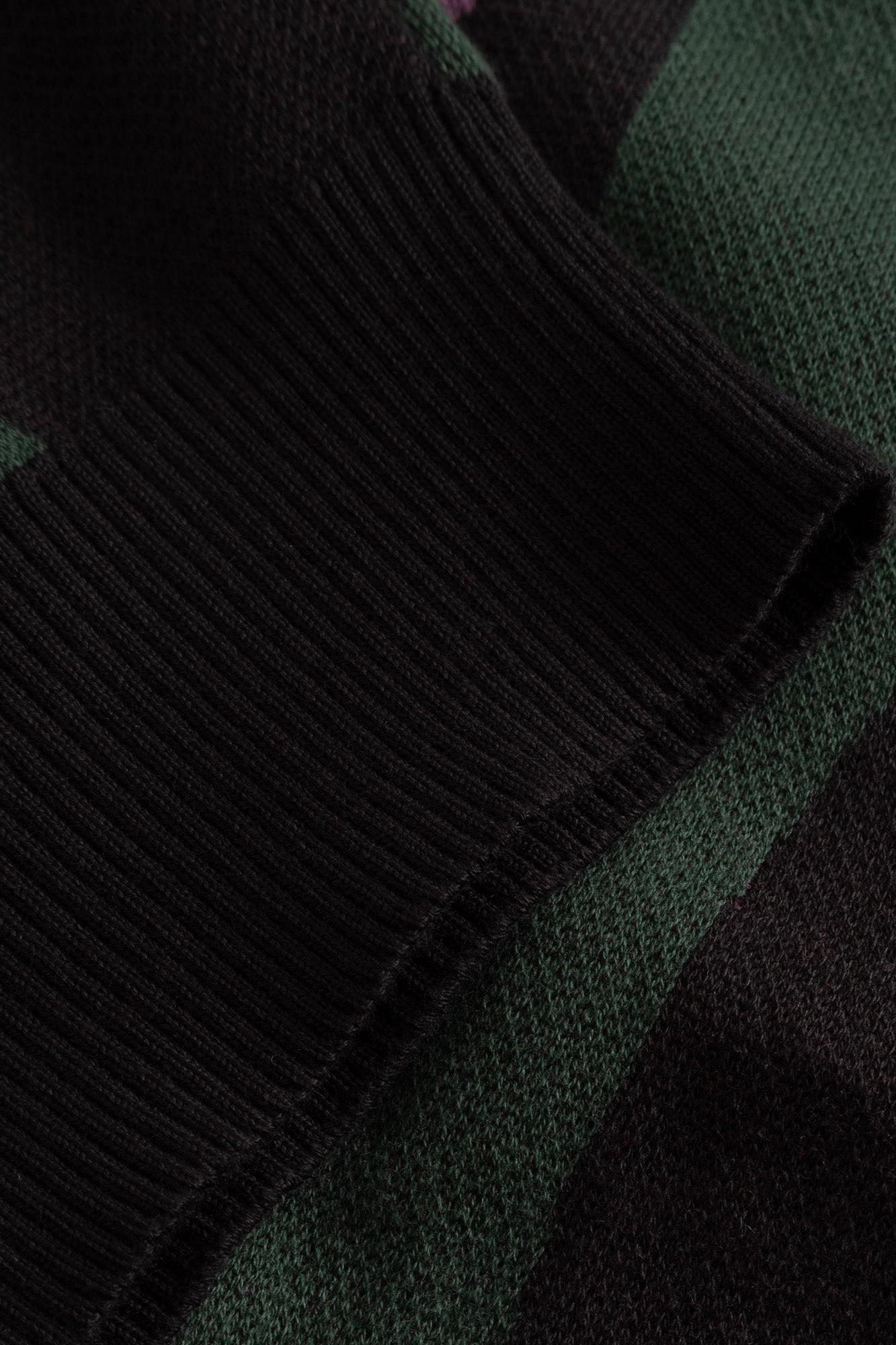 Close-up of a ribbed knit sweater or scarf in black and dark green with a subtle check pattern.