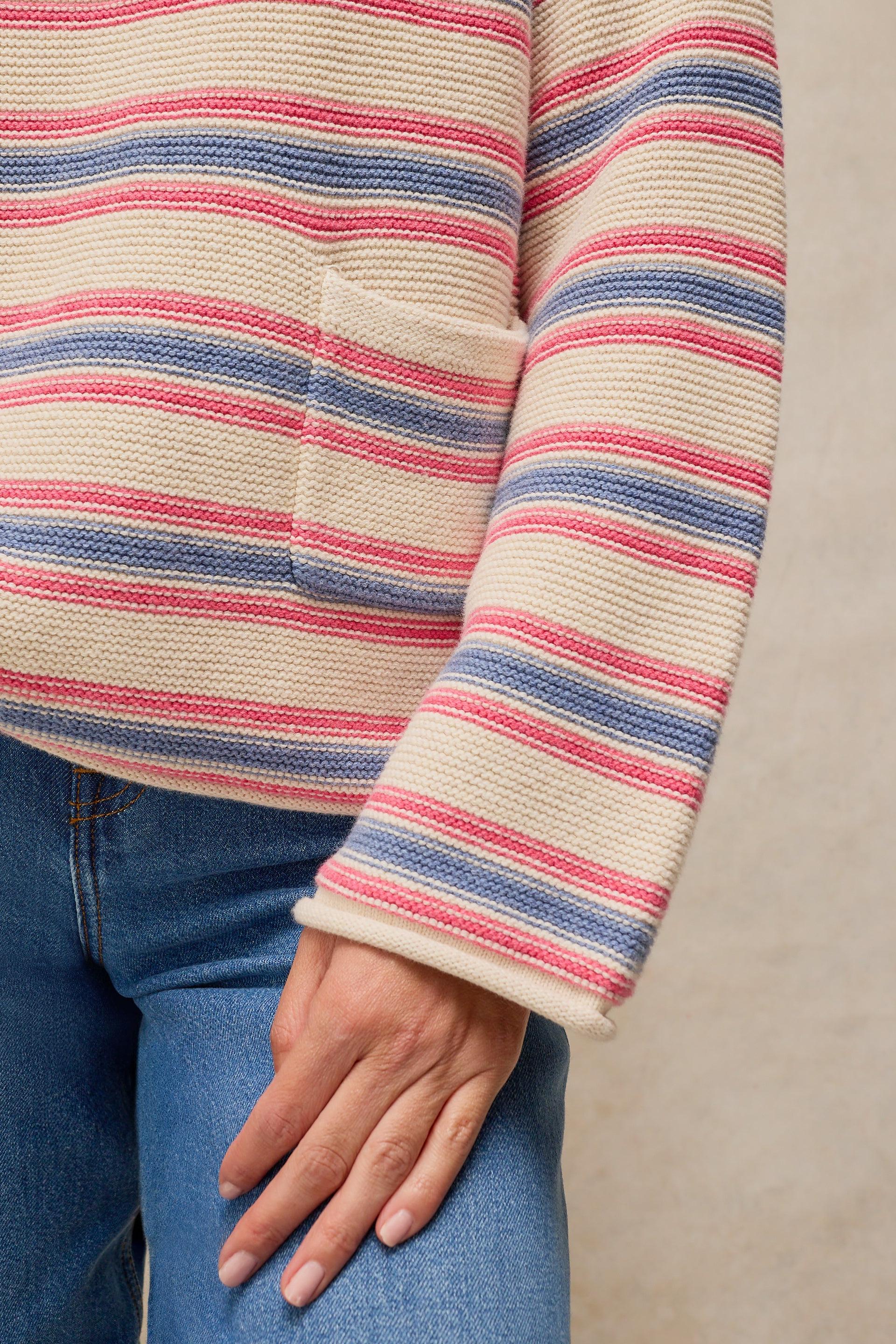 Close up of a person wearing a pink, blue, and cream striped organic cotton sweater with a patch pocket.