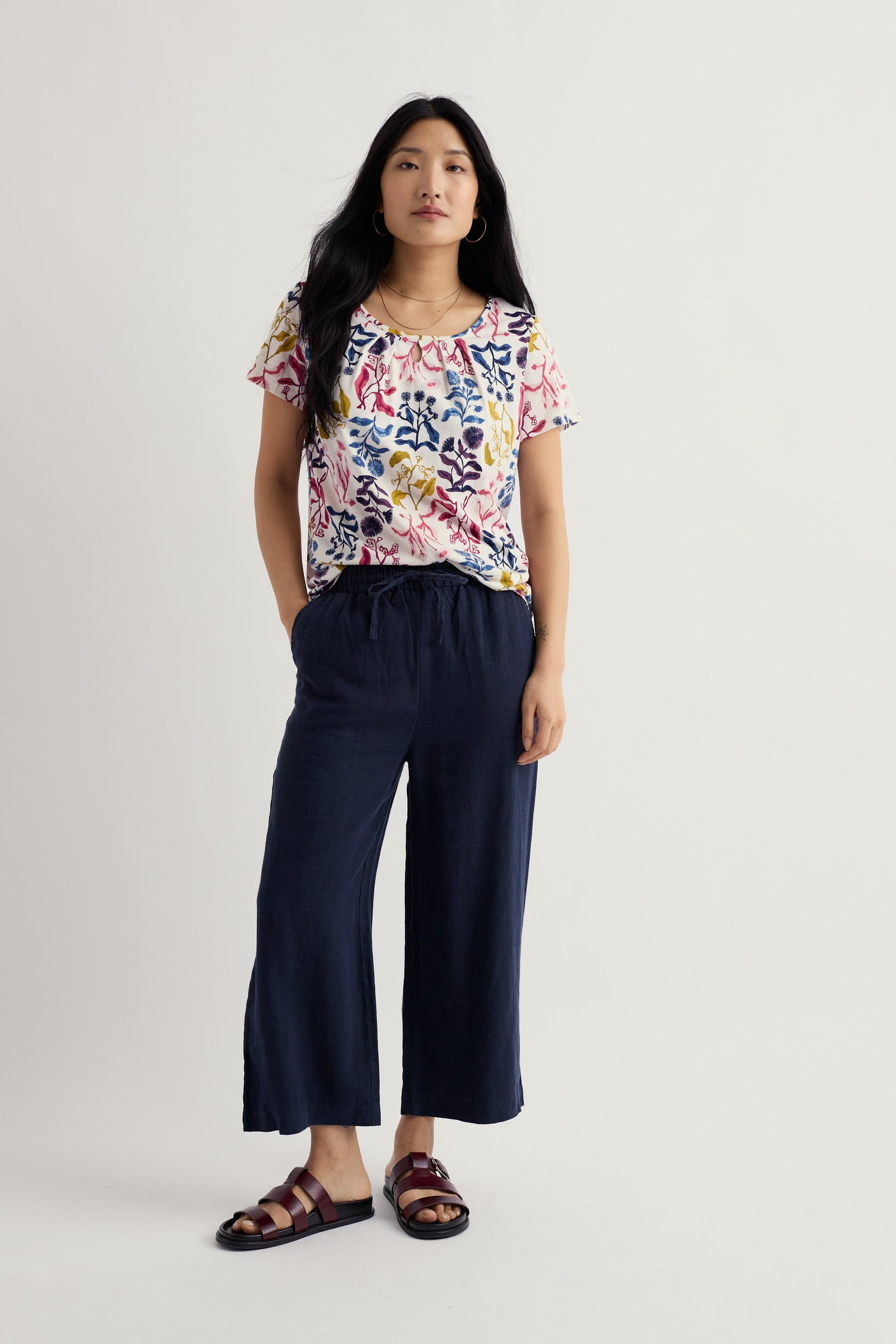 Woman wearing a floral Seasalt top and navy pants on a white background
