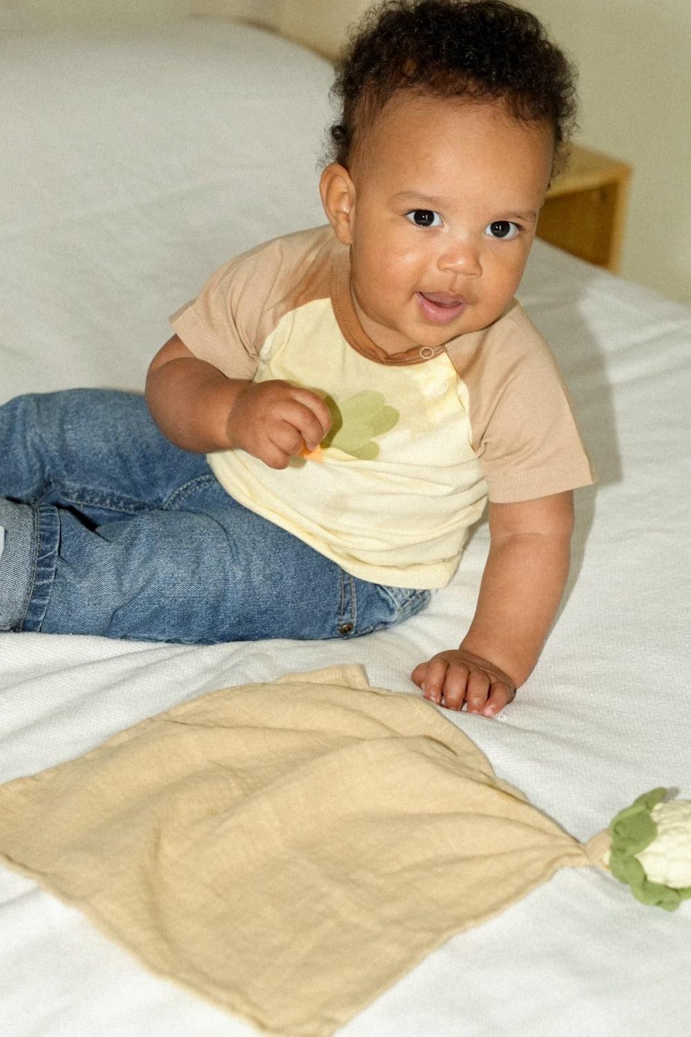 Baby lying on a bed beside organic cotton comforter.