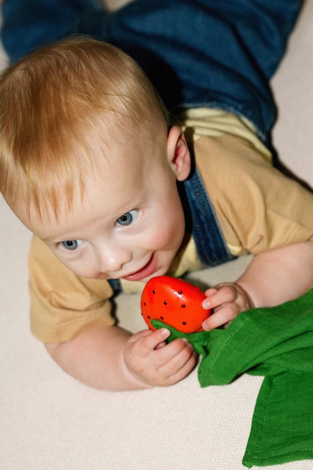 Child playing 100% natural rubber toy strawberry on organic cotton comforter.